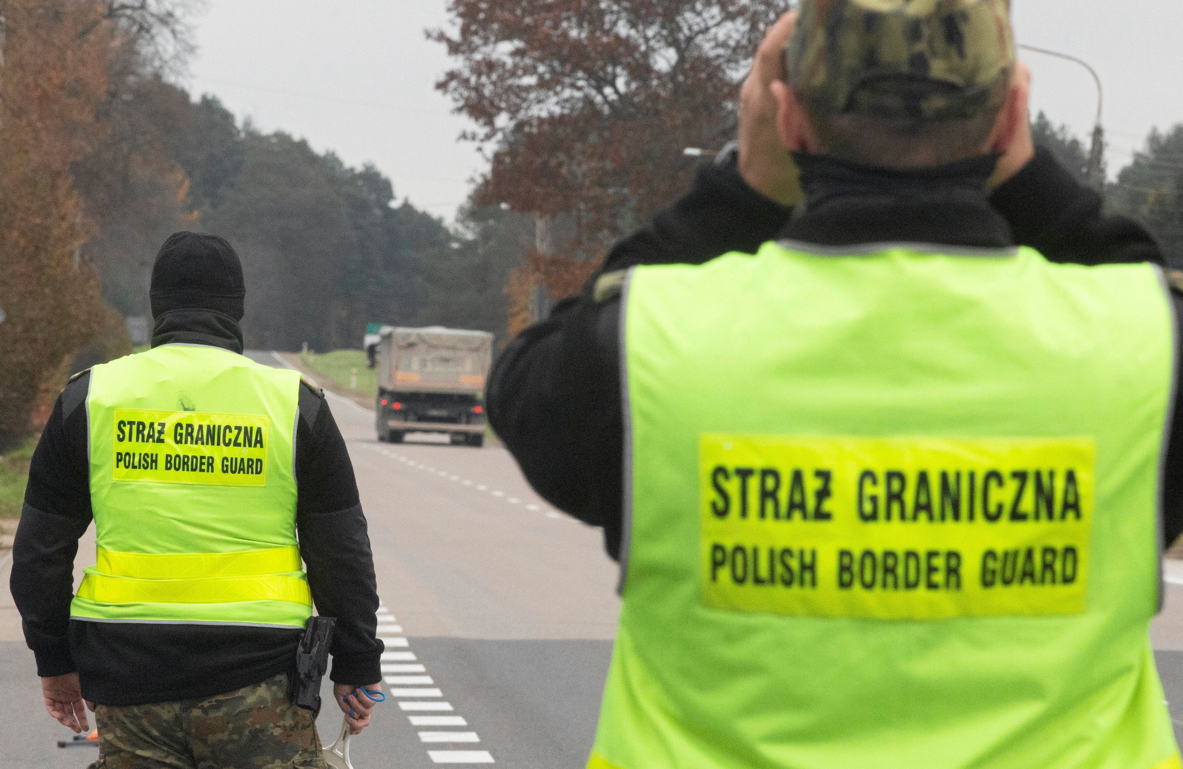 28.10.2021, Patrol Straży Granicznej na trasie S19 Białystok-Sokółka. Funkcjonariusz w żółtej kamizelce odblaskowej z napisem "Straż Graniczna. Polish Border Guard" przykłada do oczu lornetkę. W tle przejeżdżający trasą samochód