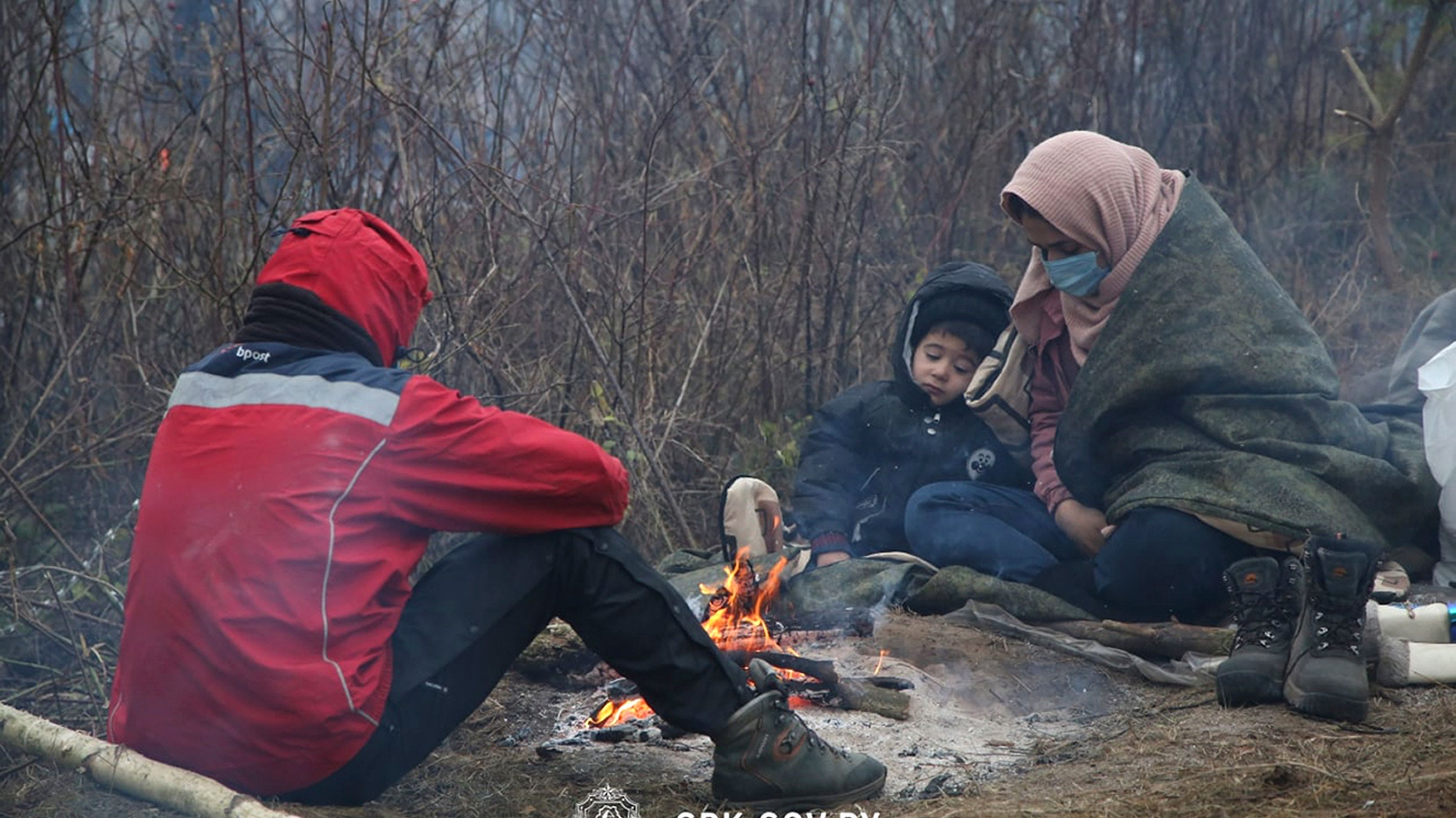 Kobieta z dzieckiem i mężczyzna siedzący na ziemi przy ognisku w chłodzie.
