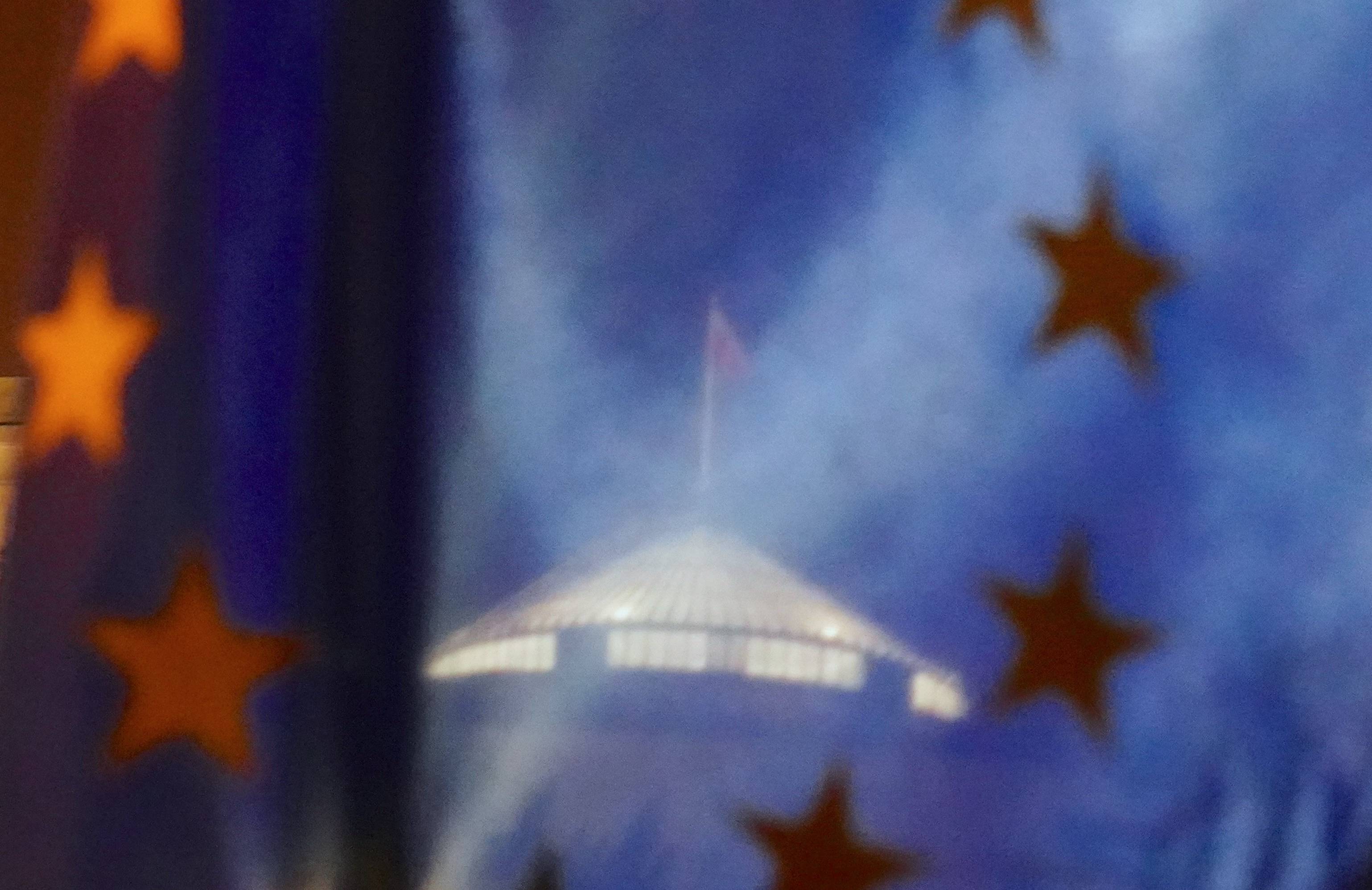 Przez europejską flagę prześwituje budynek polskiego parlamentu