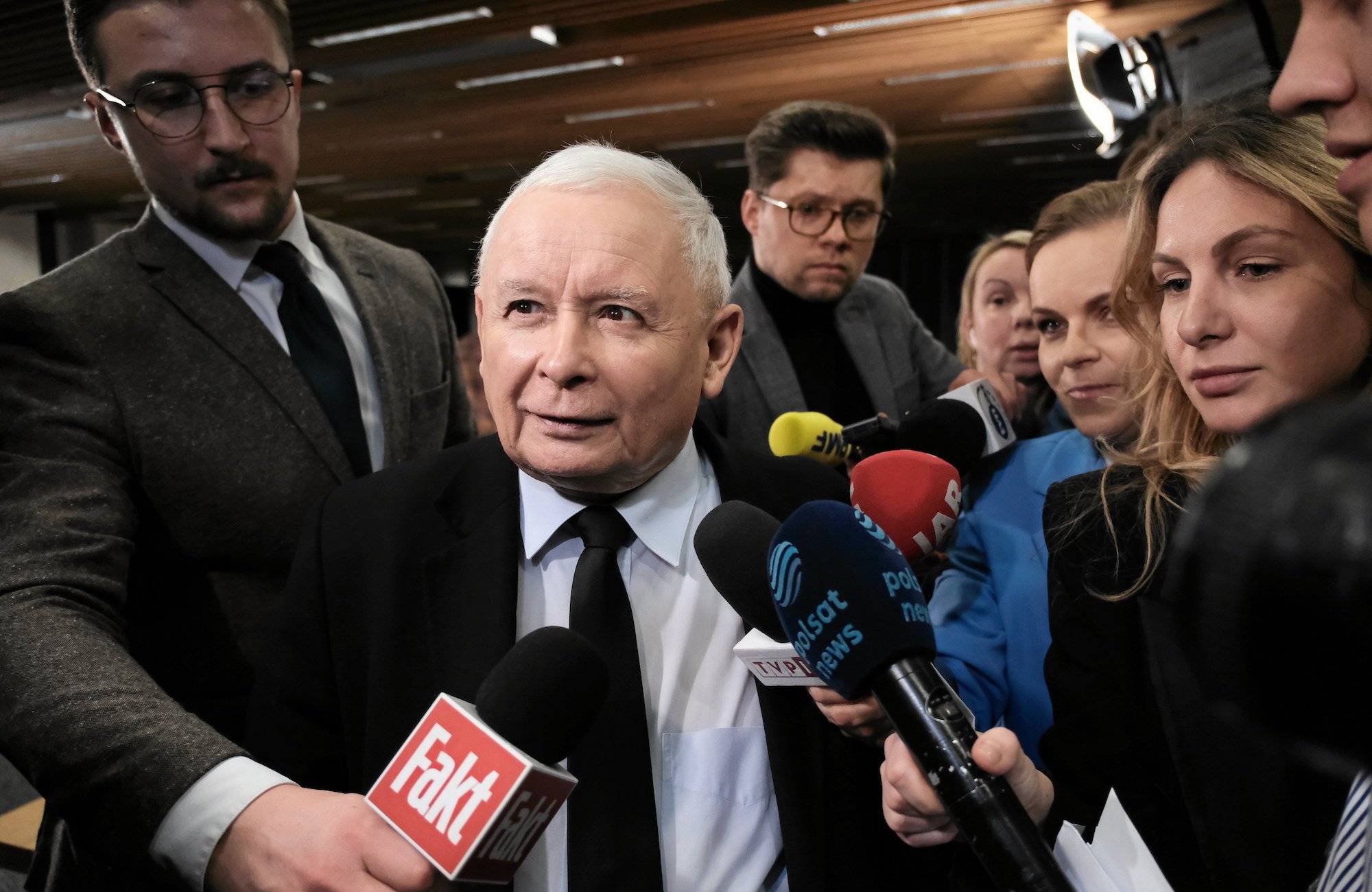 Jarosław Kaczyński otoczony przez dziennikarzy. Uśmiecha się do kamery.