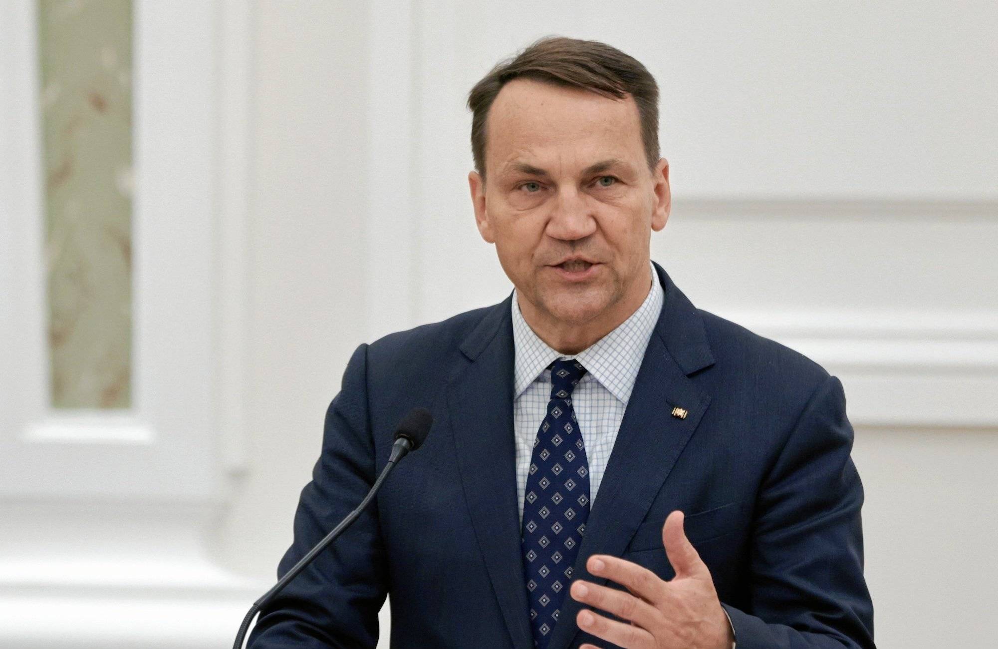 Radosław Sikorski w ciepmnym garniturze i krawacie przemawia do mikrofonu