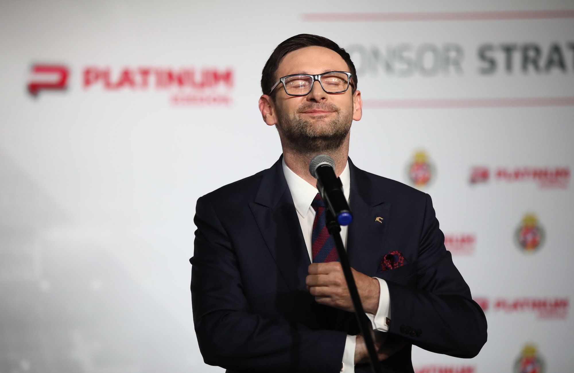 Daniel Obajtek prezes Orlenu z przymkniętymi oczami stoi przed mikrofonem