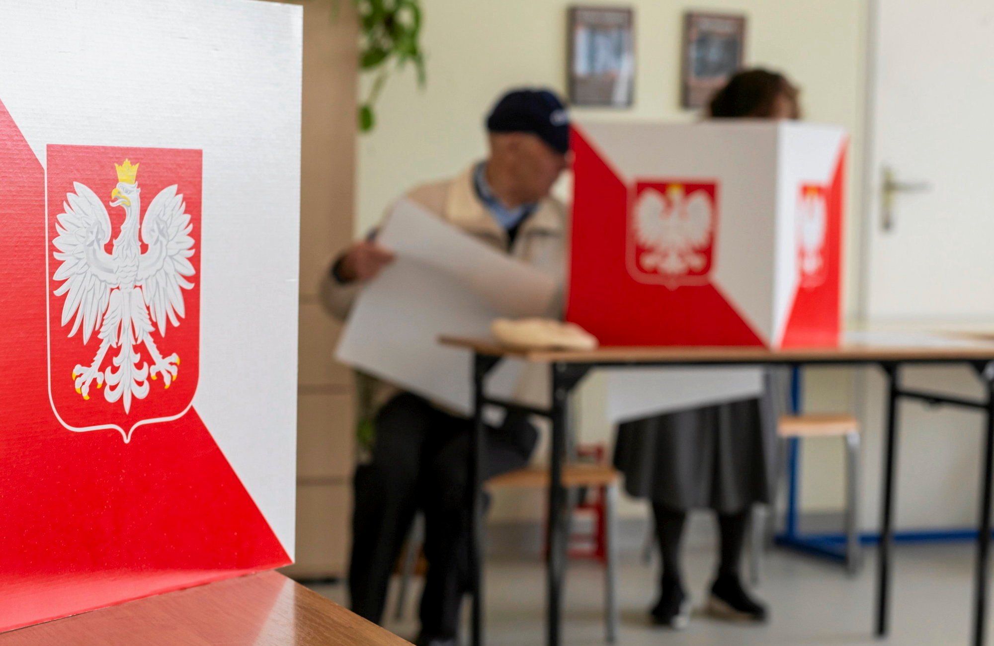 Głosowanie, osoby wypełniają karty do głosowania za parawanem biało-czerwonym