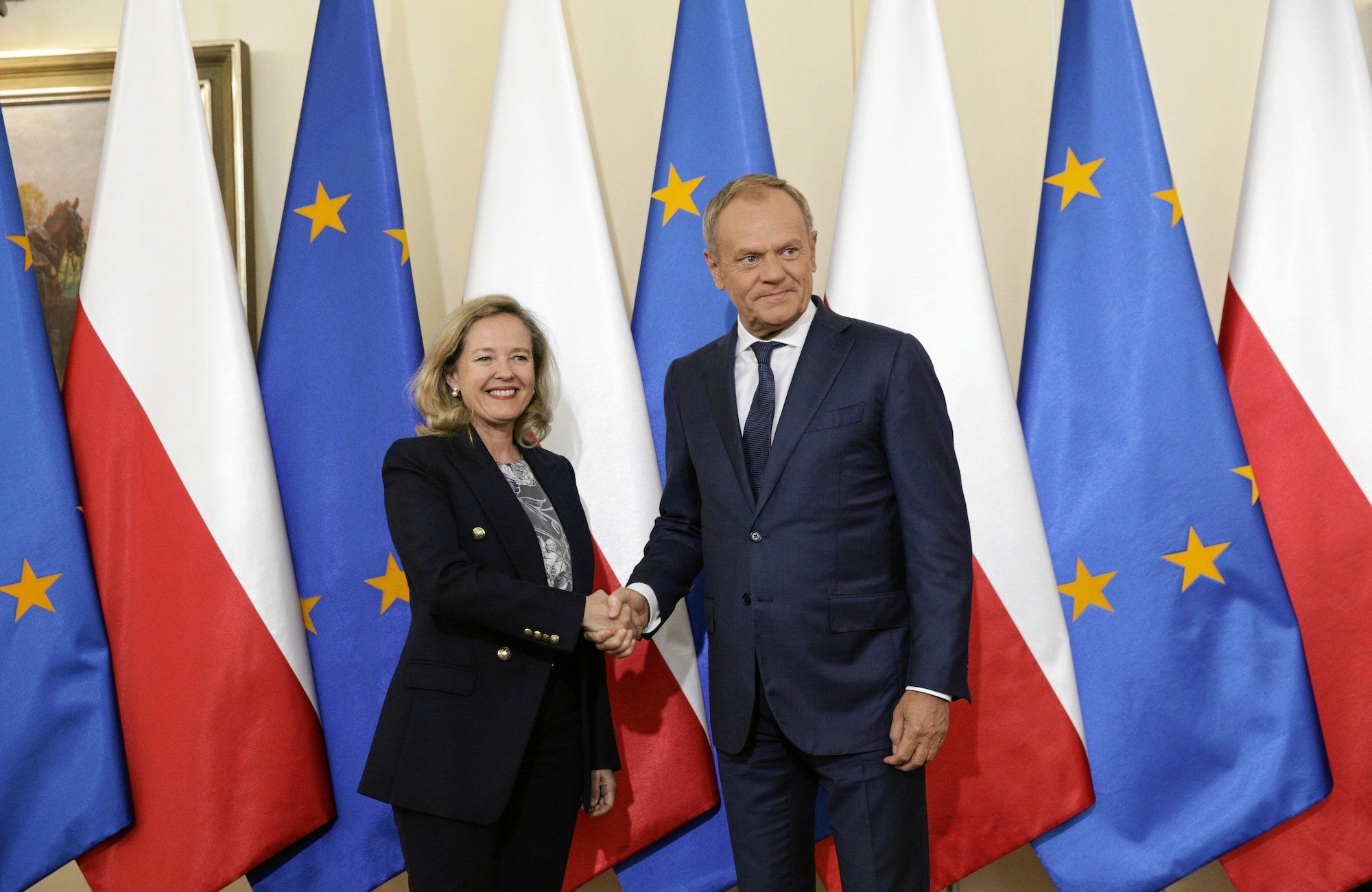 Donald Tusk i Nadia Calvino ściskają sobie ręce na tle biało-czerwonych i unijnych flag