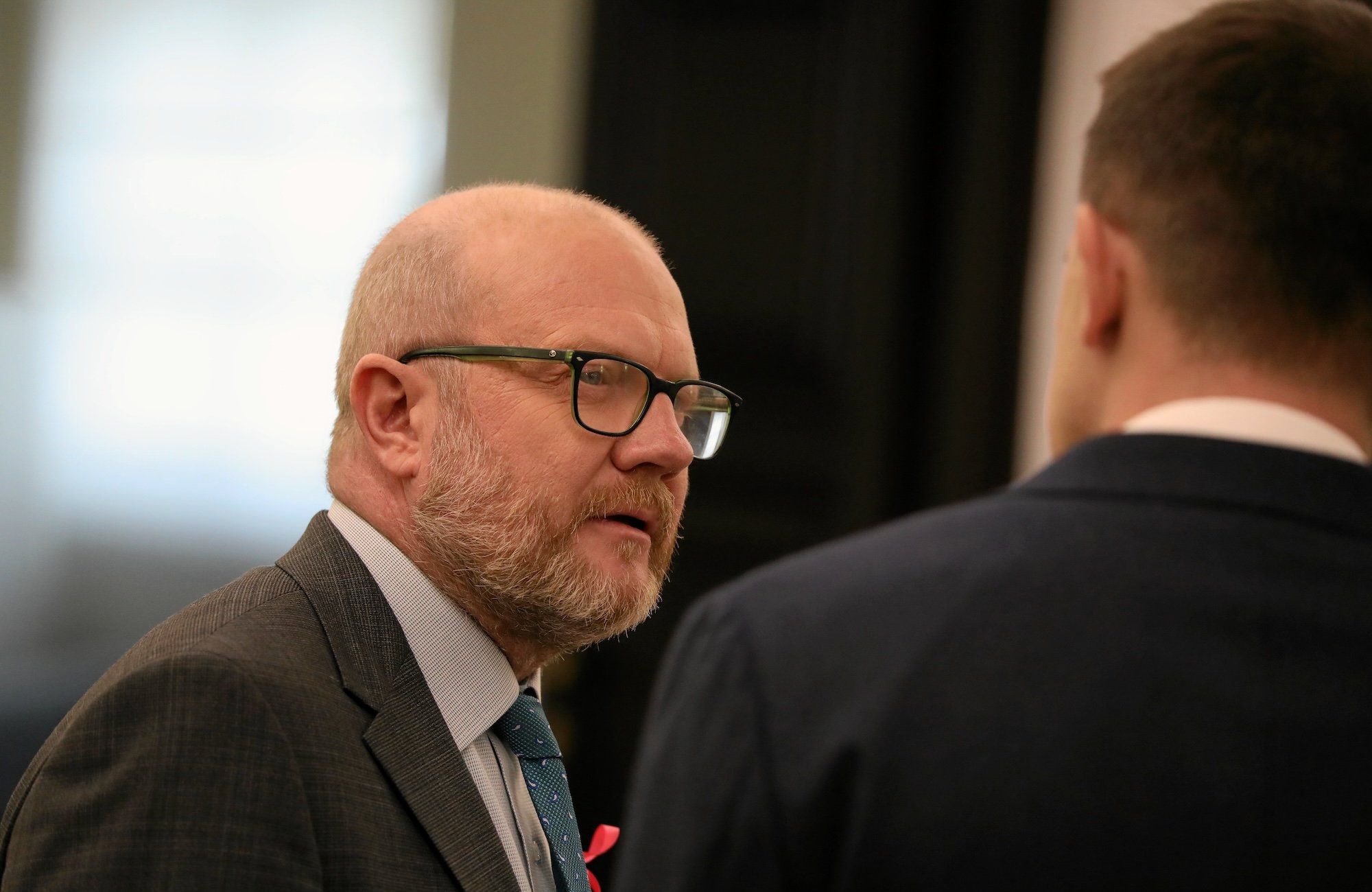 Minister Maciej Duszczyk: łysy mężczyzna w ciemnej marynarce i zielonym krawacie. Na twarzy ma kilkudniowy zarost i okulary w prostokątnych, ciemnych oprawkach