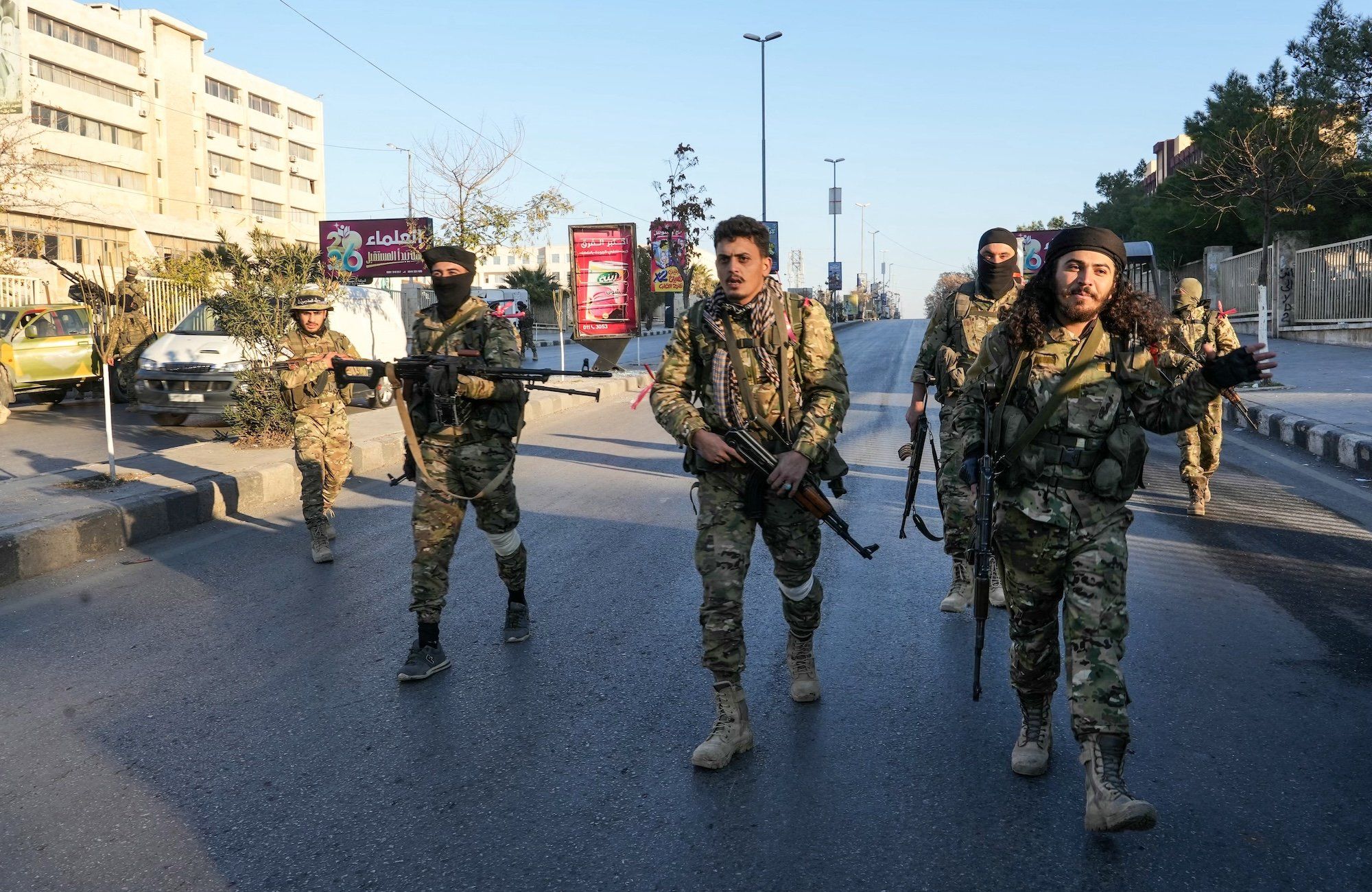 Żołnierze w mundurach moro idą ulicą Aleppo w Syrii. W ręku mają karabiny, niektórzy na głowach kominiarki
