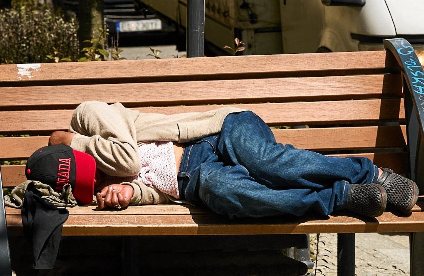 Mężczyzna w czapce z daszkeim śpi na ławce. Obok puszka piwa.