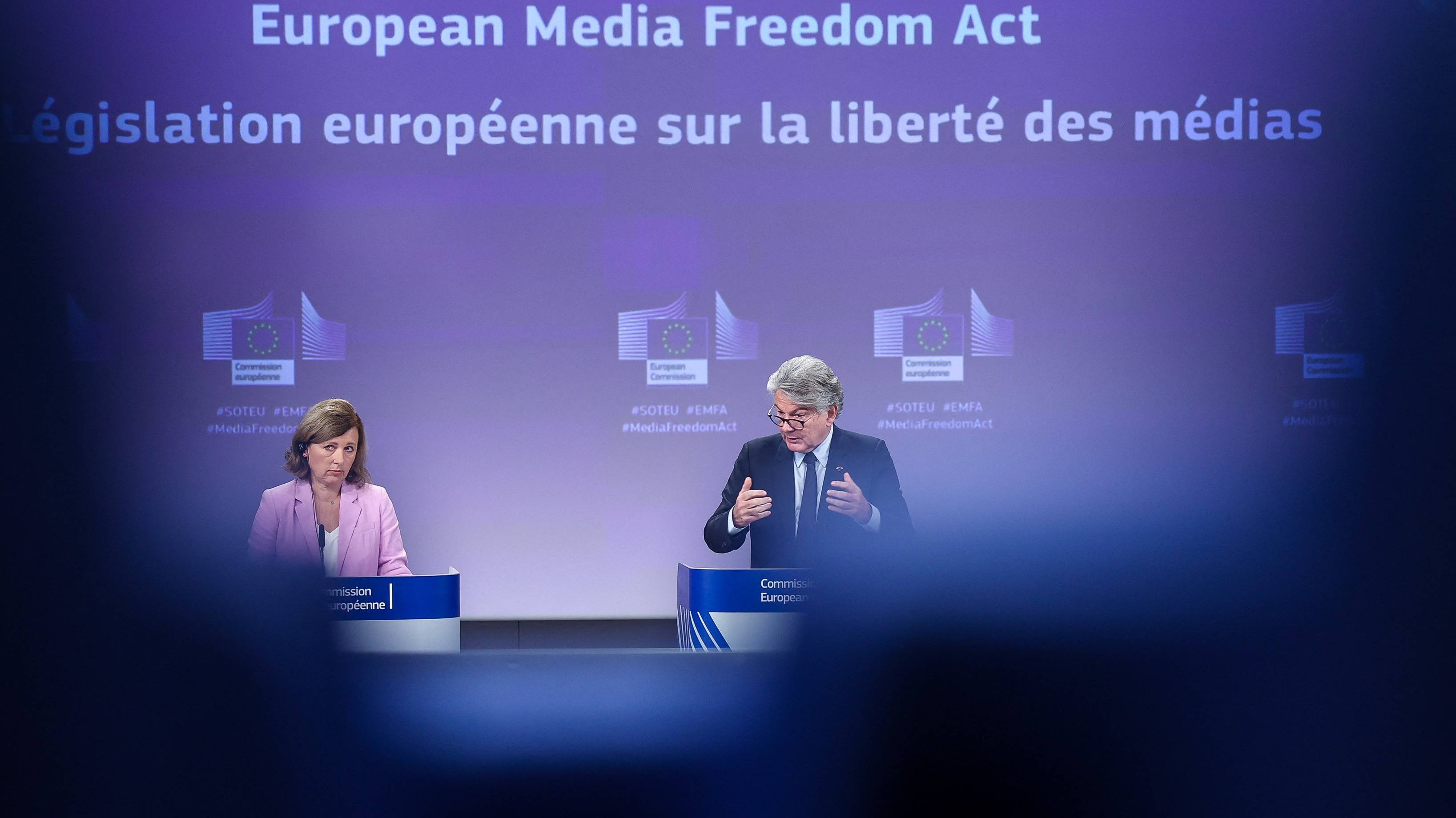 Dwoje polityków i napis na niebieskiej tablicy po angielsku i francusku (Europejski Akt o Wolności Mediów)