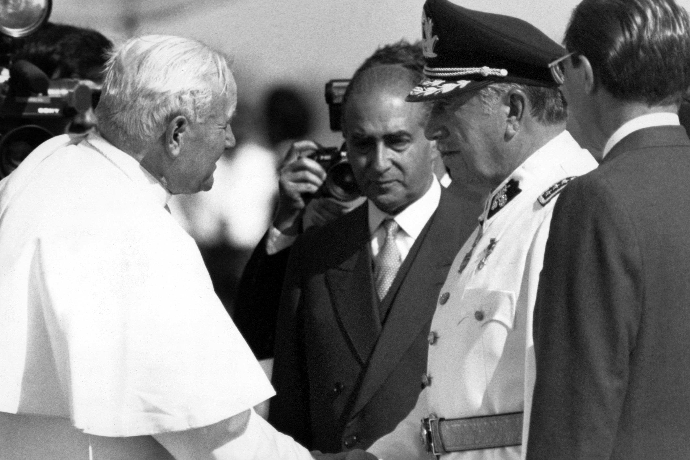 Papież Jan Paweł II ściska rękę dyktatora Chile Augusto Pinocheta, w otoczeniu urzędników w garniturach.