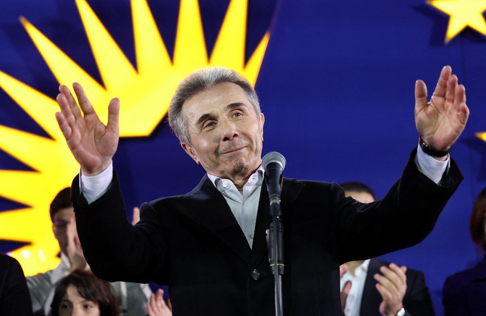 Gruziński oligarcha Bidzina Iwaniszwili podczas przemówienia po ogłoszeniu wyników wyborów w Gruzji. Unosi w górę obie ręce i uśmiecha się.