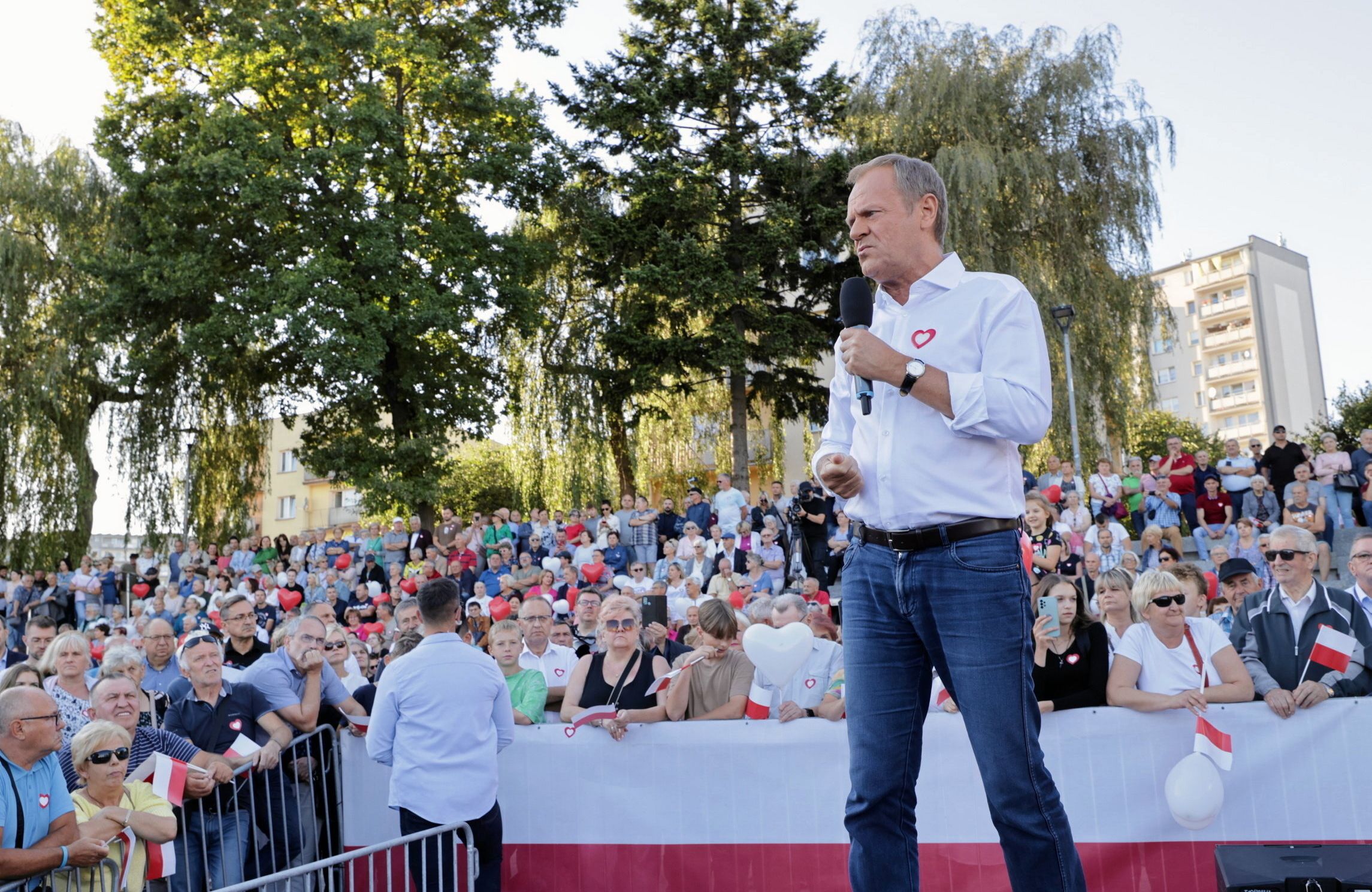 60-latek w białej koszuli i dżinsach przemawia do tłumu