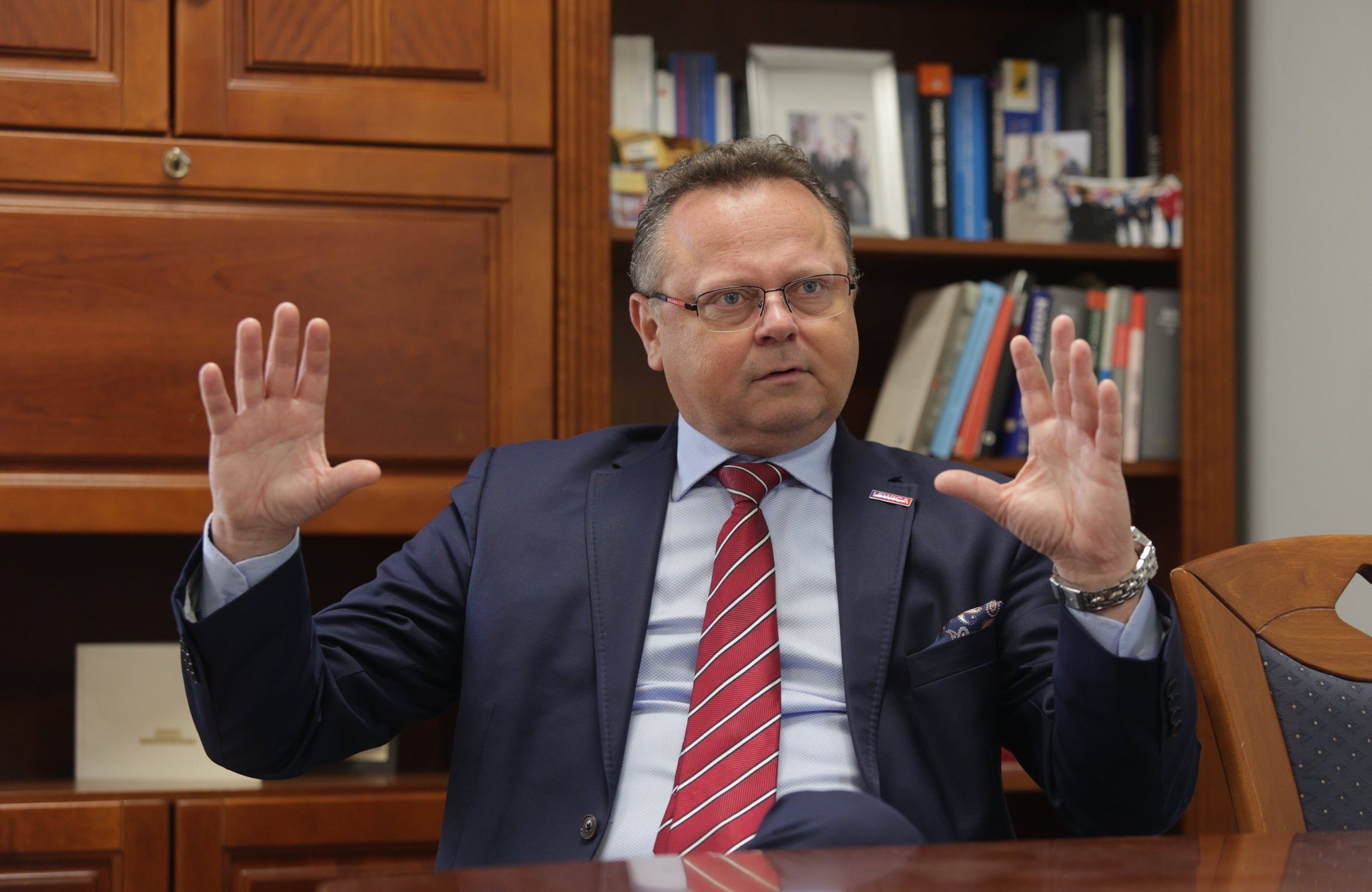 Wiceminister spraw zagranicznych Andrzej Szejna rozkłada ręce, siedzi w garniturze i czerwonym krawacie