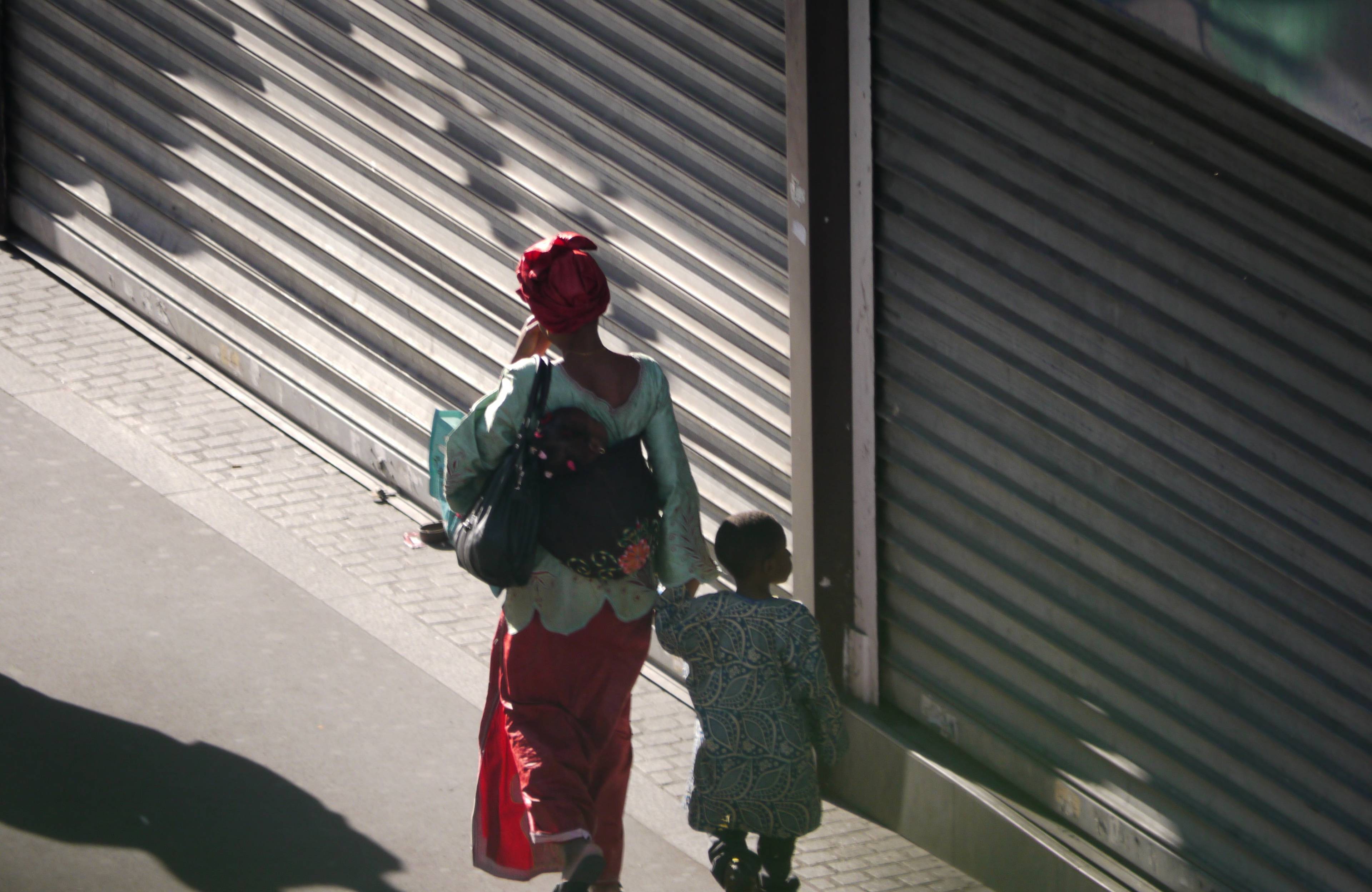Czarnoskóra kobieta z dzieckiem idzie obok zamkniętych witryn sklepów