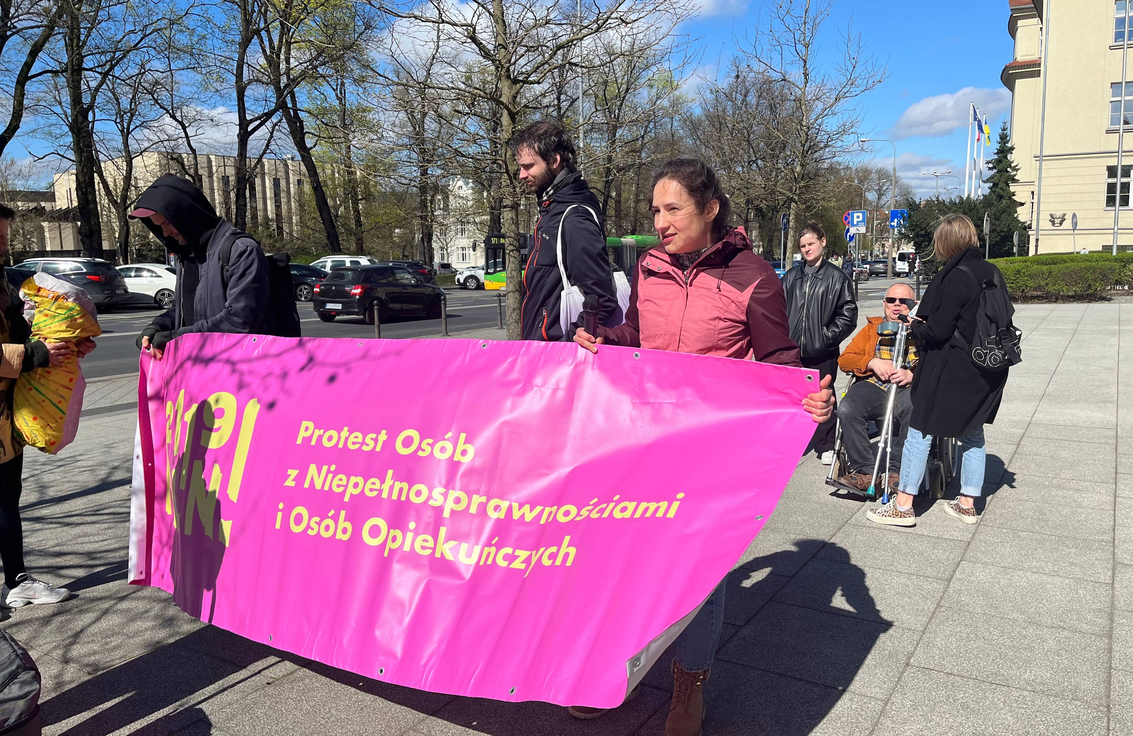 Ludzie z różowym plakatem protestujących osób z niepełnosprawnościami