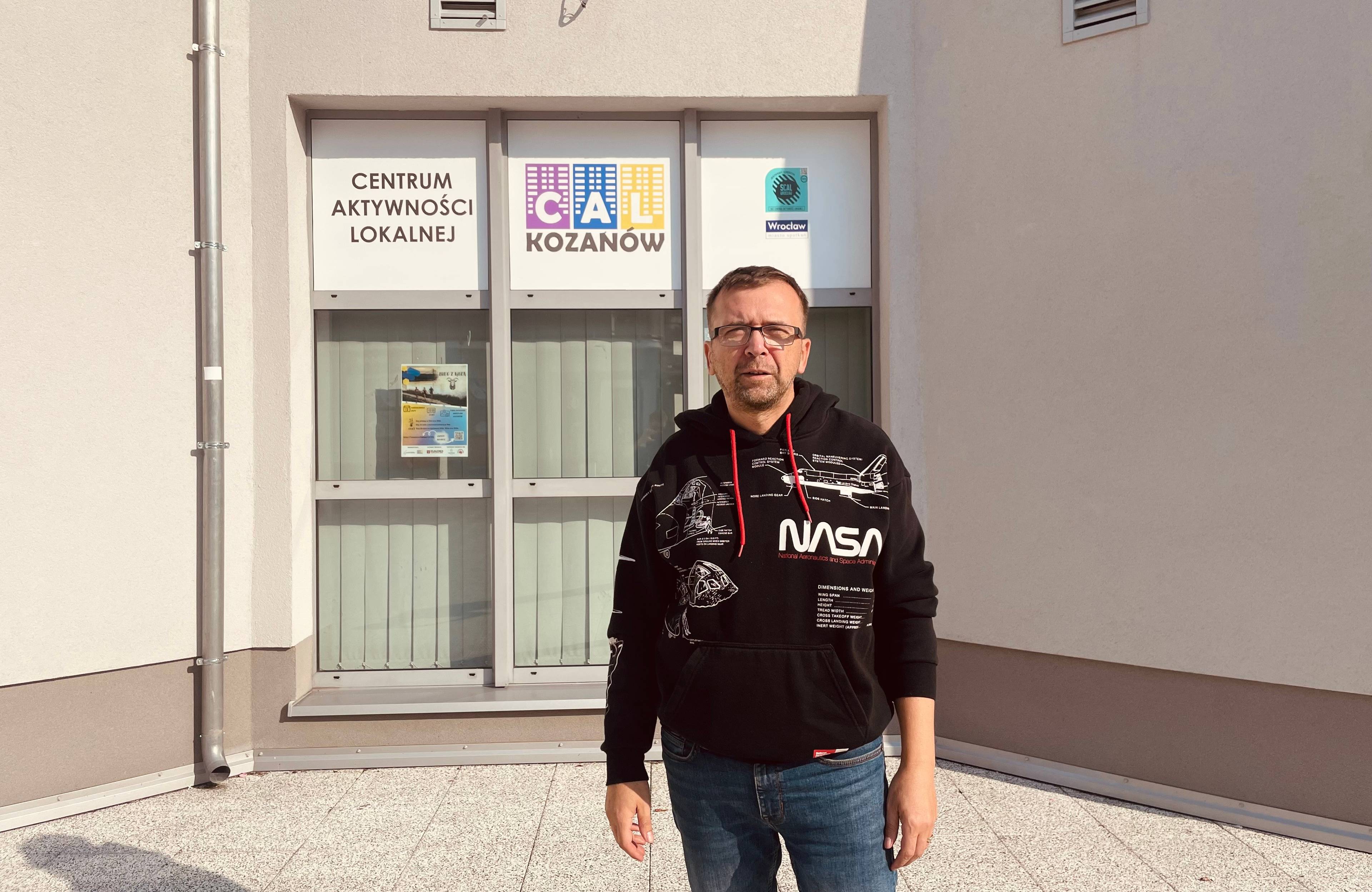 40-letni mężczyzna w sportowym stroju przed budynkiem Centrum Aktywności Lokalnej