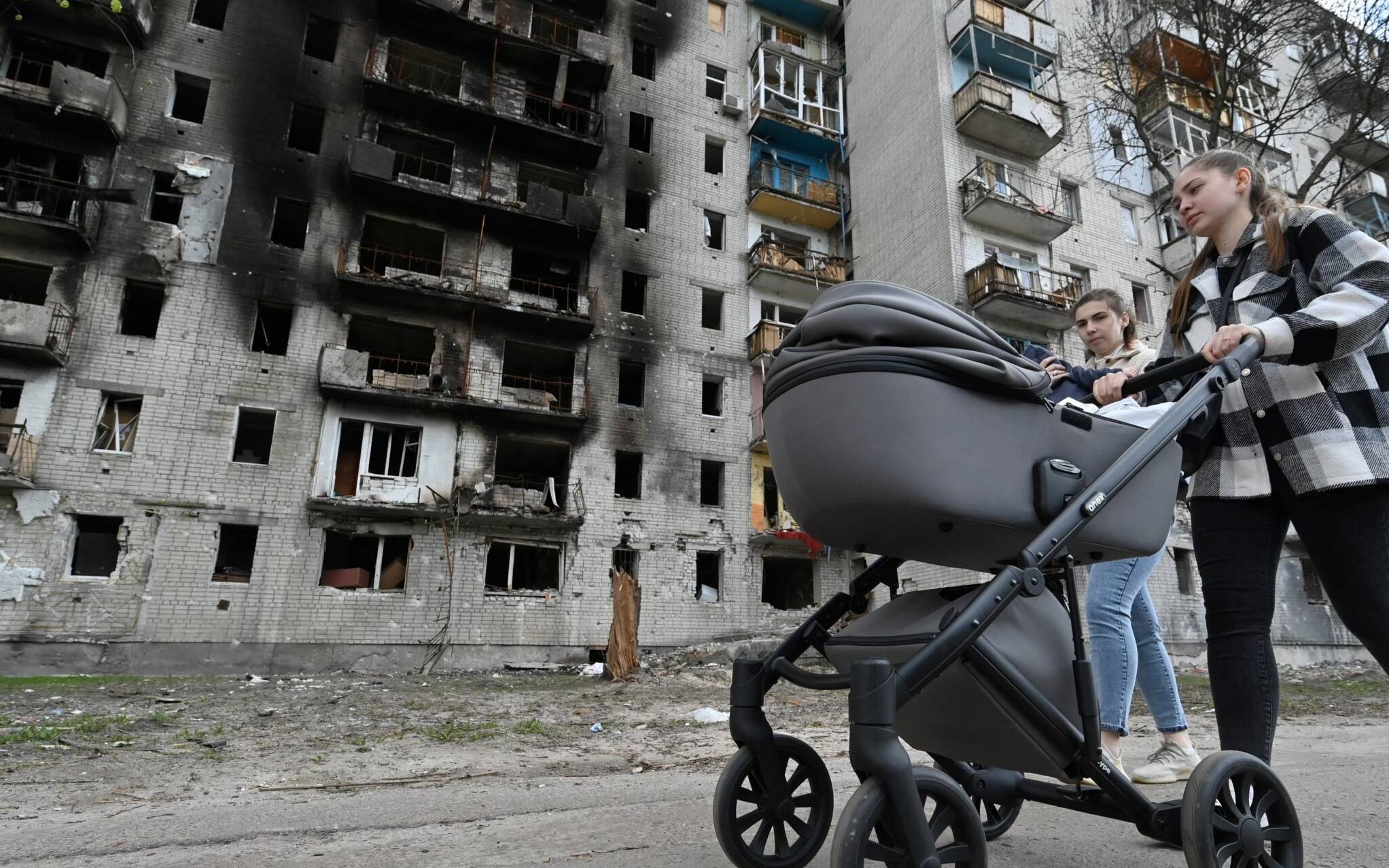 A woman pushes a pram past a heavily damaged residential building in the northern Ukrainian city of Chernigiv on May 3, 2022, amid the Russian invasion of Ukraine. - Russia's withdrawal from Chernigiv after a month-long assault left behind a devastated city that Ukraine will needs massive foreign aid, and many years of work, to restore. (Photo by Genya SAVILOV / AFP)