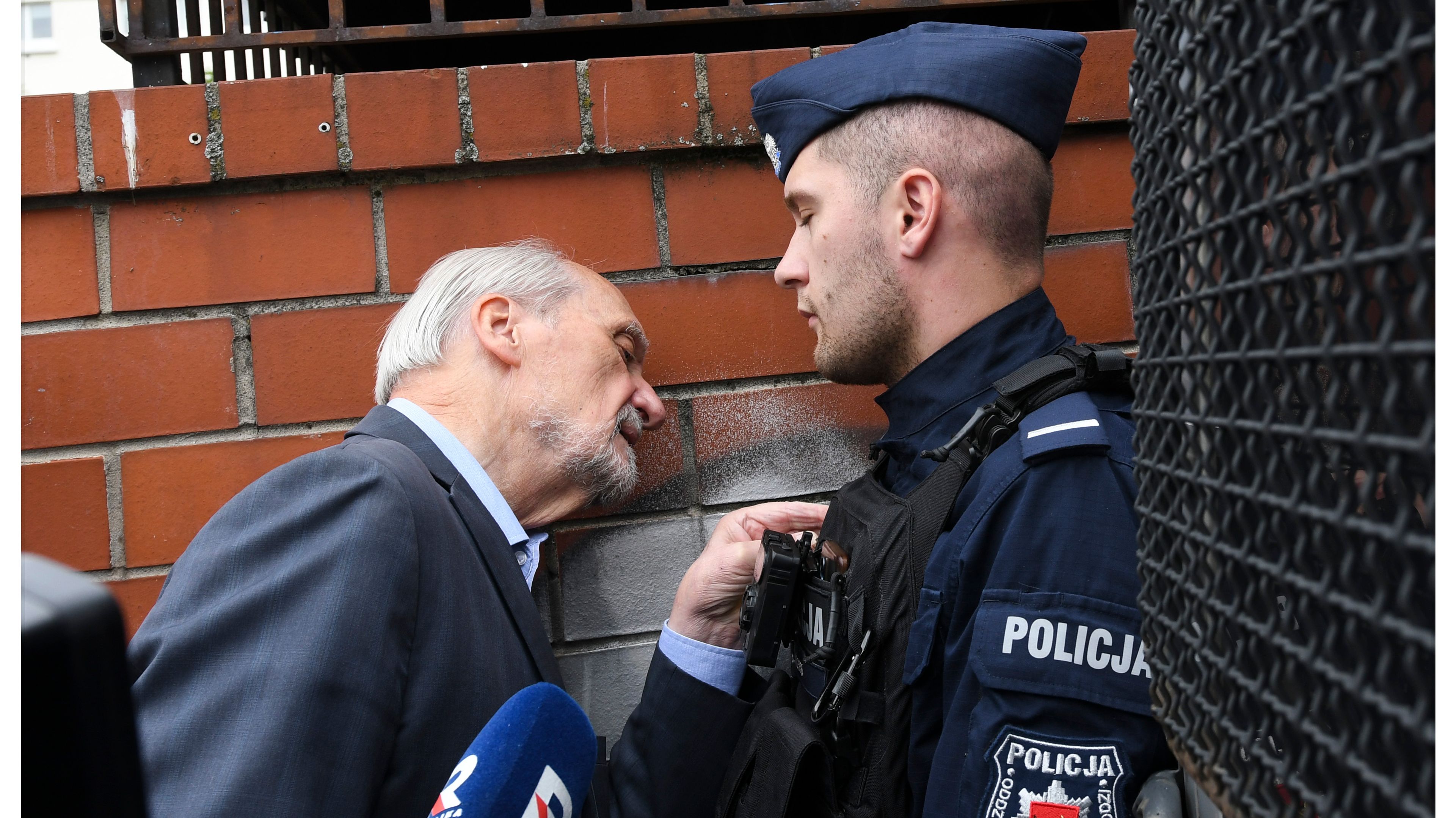 Policjant zagradza przejście siwemu mężczyźnie.