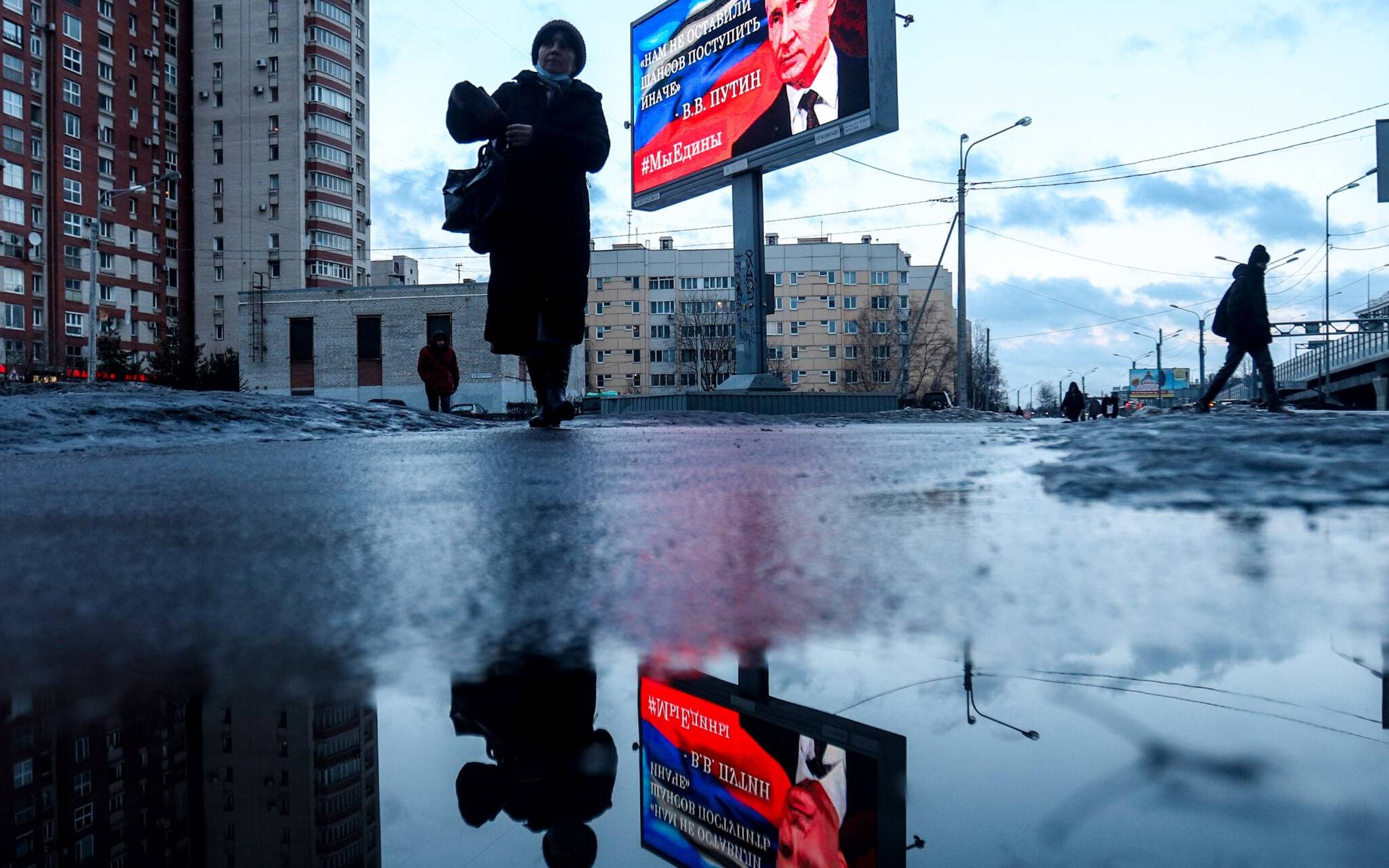Pedestrians walk past a board displaying an image of Russian President Vladimir Putin and a quote from the recent his address to the nation: "We had no other chance but to act differently" in Saint Petersburg, on February 25, 2022. (Photo by Sergei MIKHAILICHENKO / AFP)