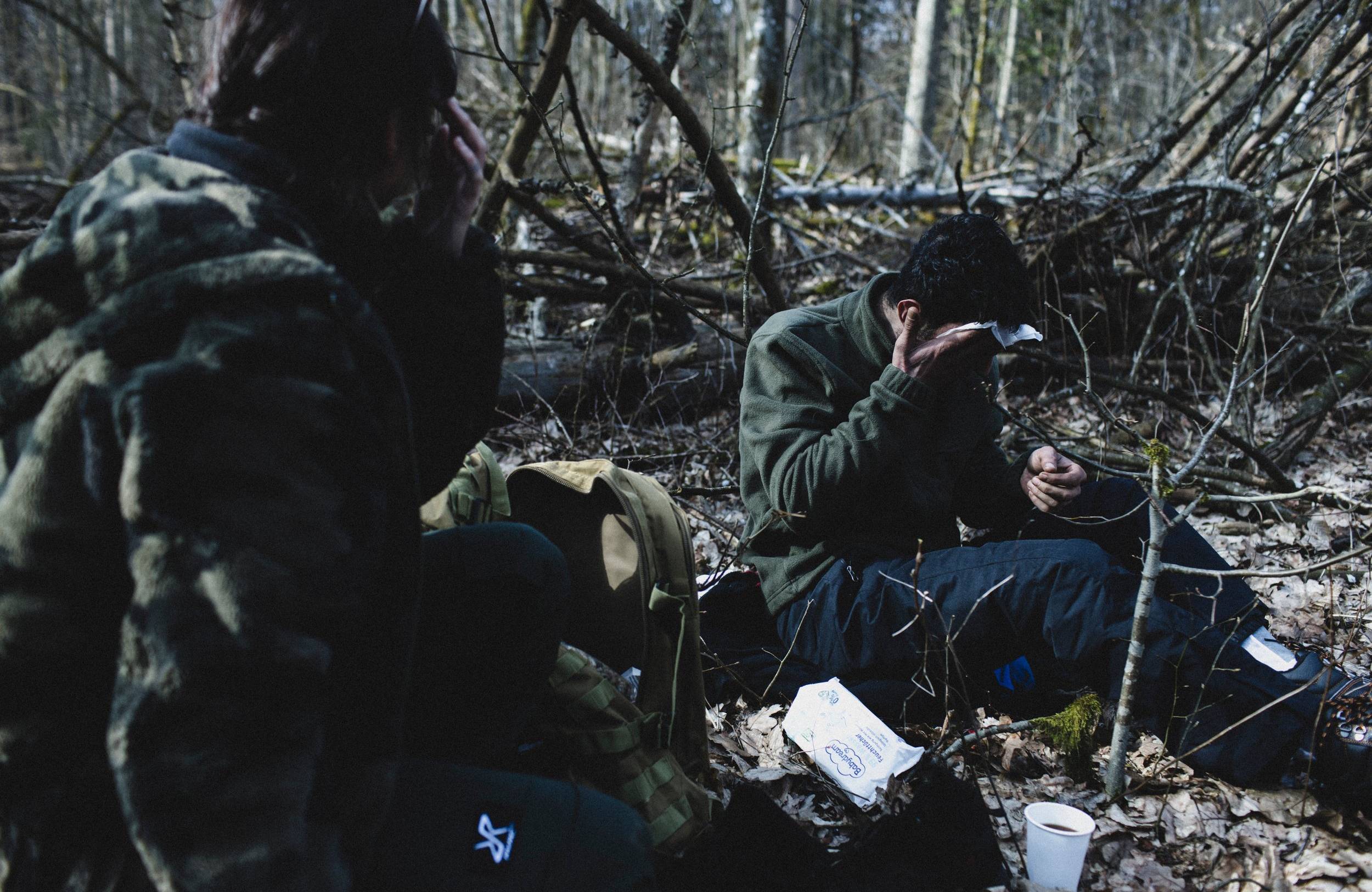 Dwaj uchodżcy siedzą w lesie, jeden z nich wyciera chusteczką higieniczną twarz, drugi okrywa się kocem. Granica