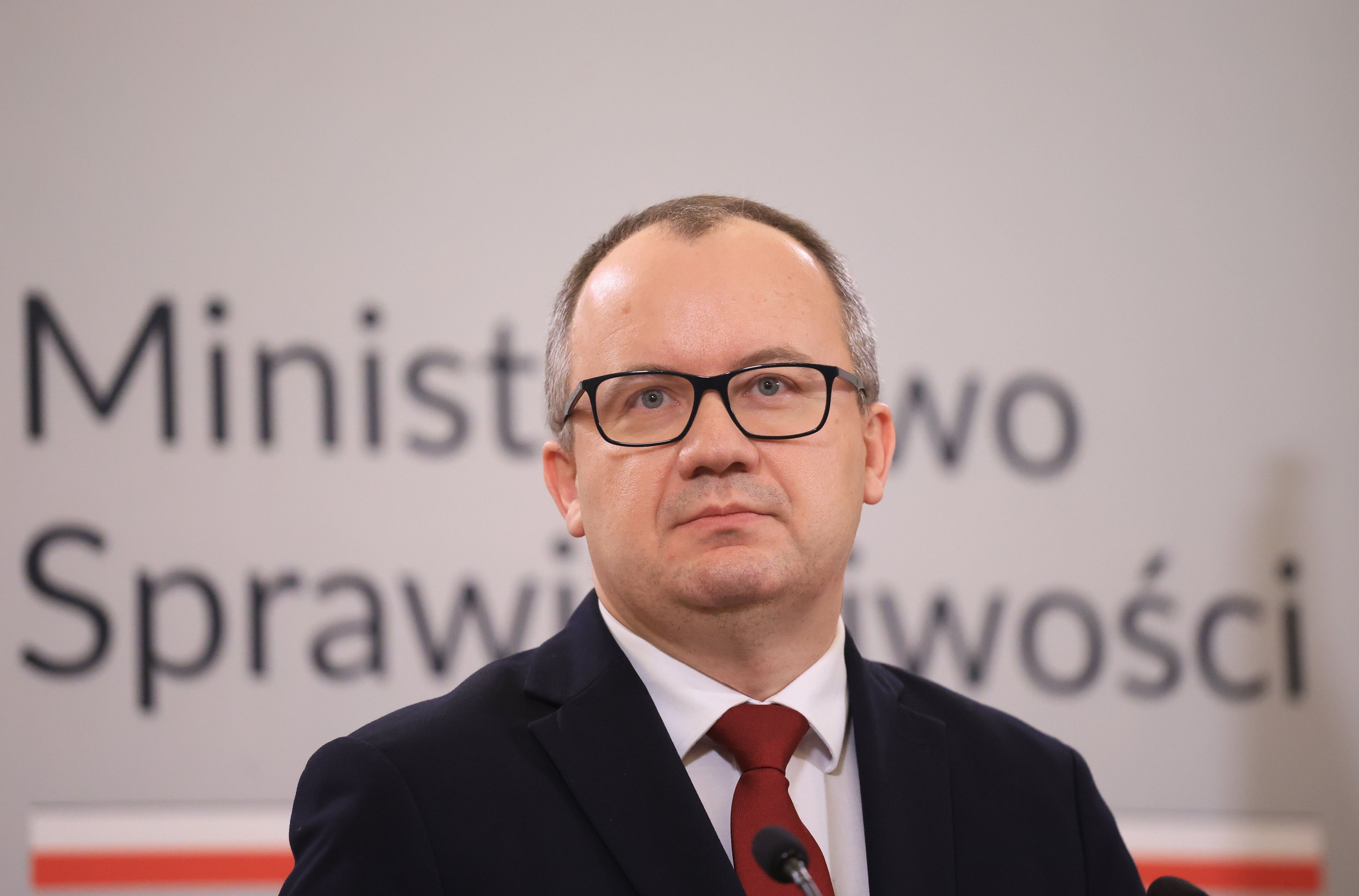 Mężczyzna w okularach na tle logo ministerstwa sprawiedliwości