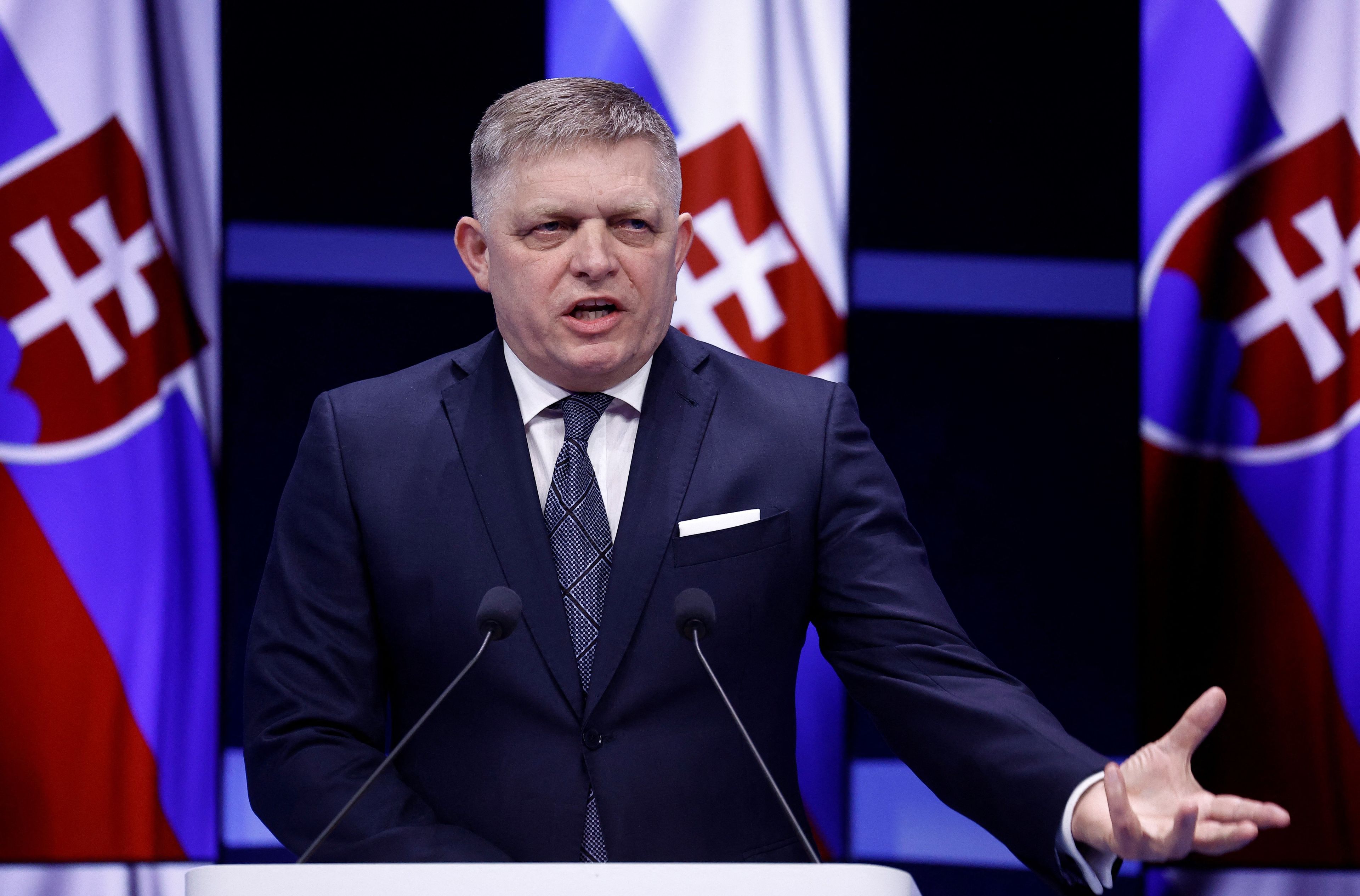 Mężczyzna w garniturze przemawia na tle flag Słowacji