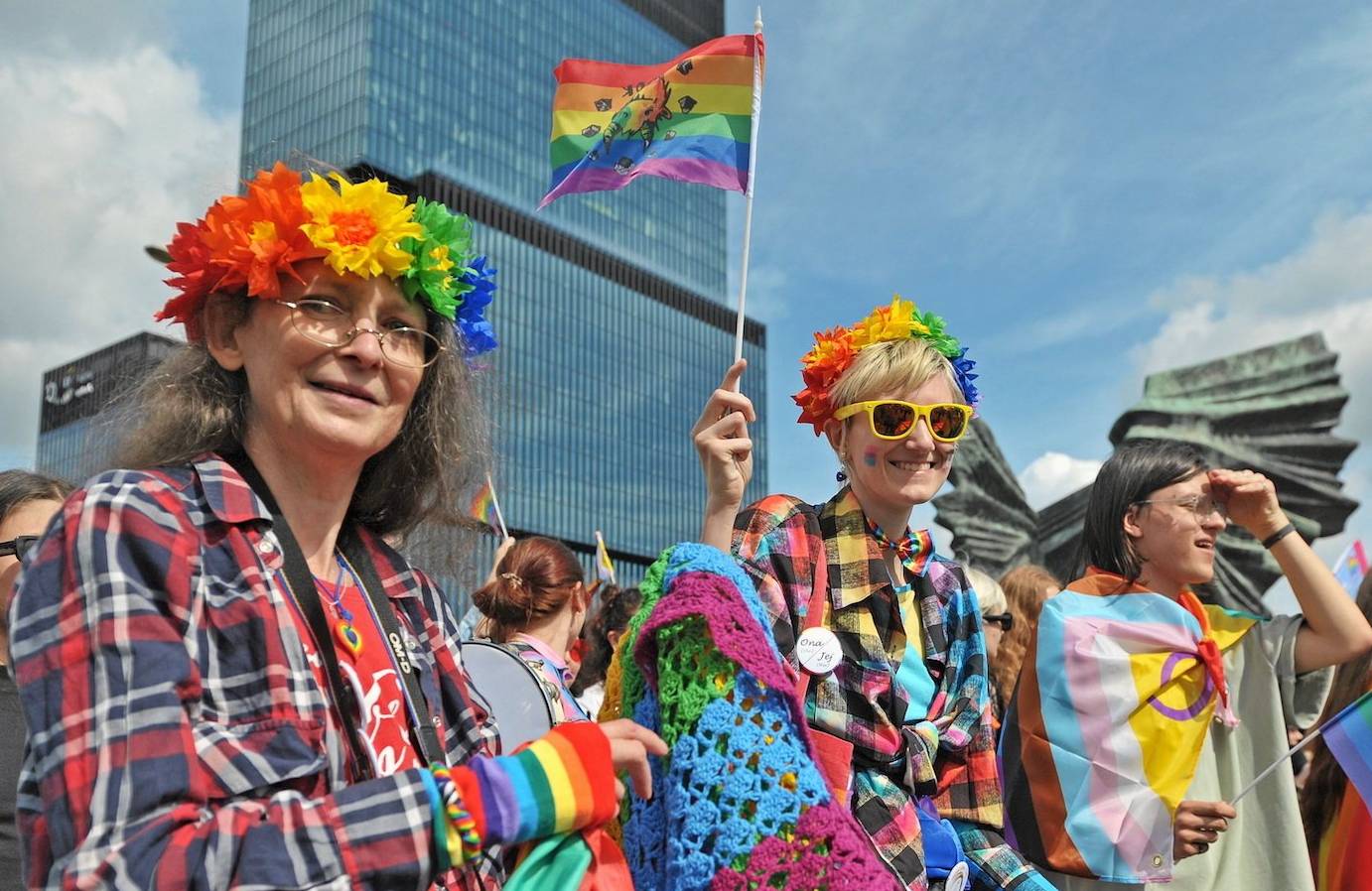 Uczestniczki parady równości w Katowicach, ubrane w kolorowe ubrania, niosą tęczowe flagi i uśmiechają się