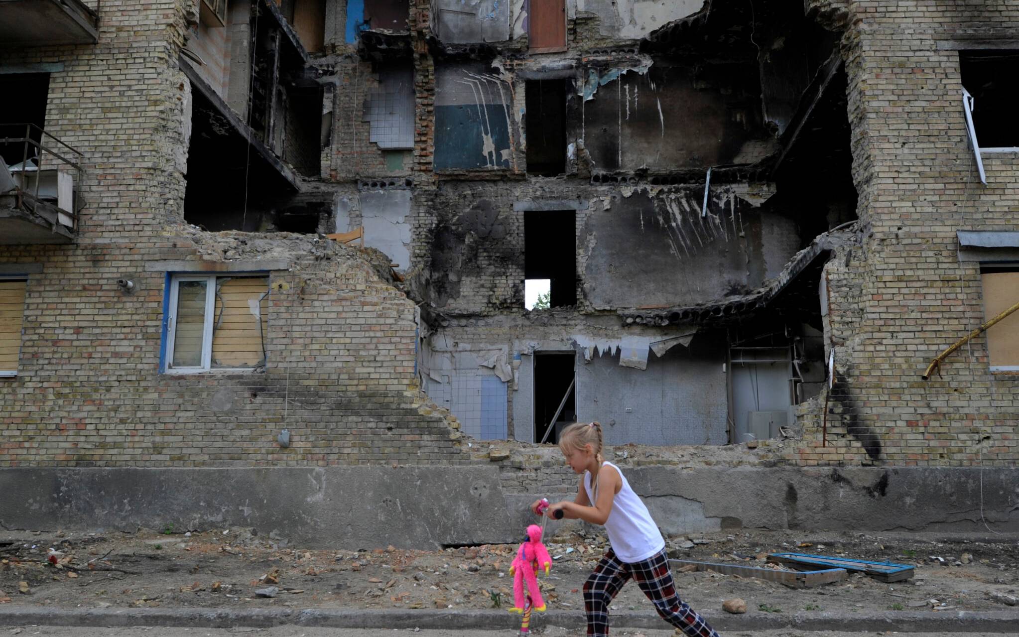 A girl rides a kick scooter past a destroyed residential building in the village of Horenka, Kyiv region, on June 4, 2022 amid the Russian invasion of Ukraine. (Photo by Sergei CHUZAVKOV / AFP)