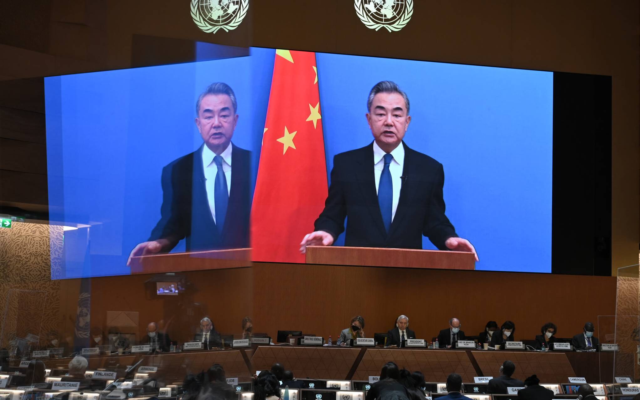 Chinese Foreign minister Wang Yi appears on a screen as he delivers a remote speech at the opening of a session of the UN Human Rights Council, following the Russian invasion in Ukraine, in Geneva, on February 28, 2022. - The UN Human Rights Council voted to hold an urgent debate about Russia's deadly invasion of Ukraine at Kyiv's request, amid widespread international condemnation of Moscow's attack. (Photo by Fabrice COFFRINI / AFP)