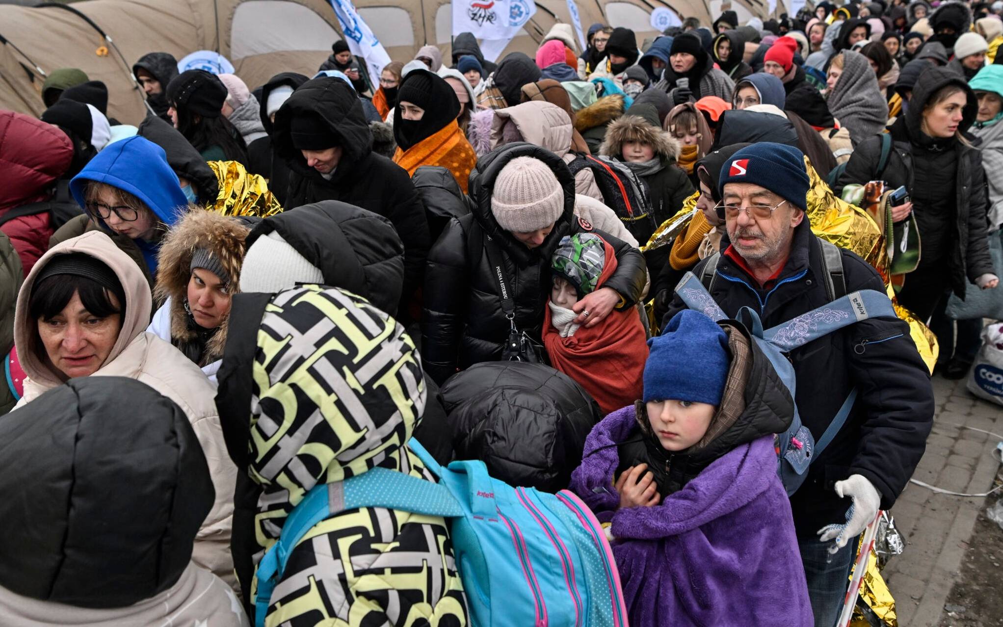 Refugees stand in line in the cold as they wait to be transferred to a train station after crossing the Ukrainian border into Poland, at the Medyka border crossing in Poland, on March 7, 2022. - More than 1.5 million people have fled Ukraine since the start of the Russian invasion, according to the latest UN data on March 6, 2022. (Photo by Louisa GOULIAMAKI / AFP)