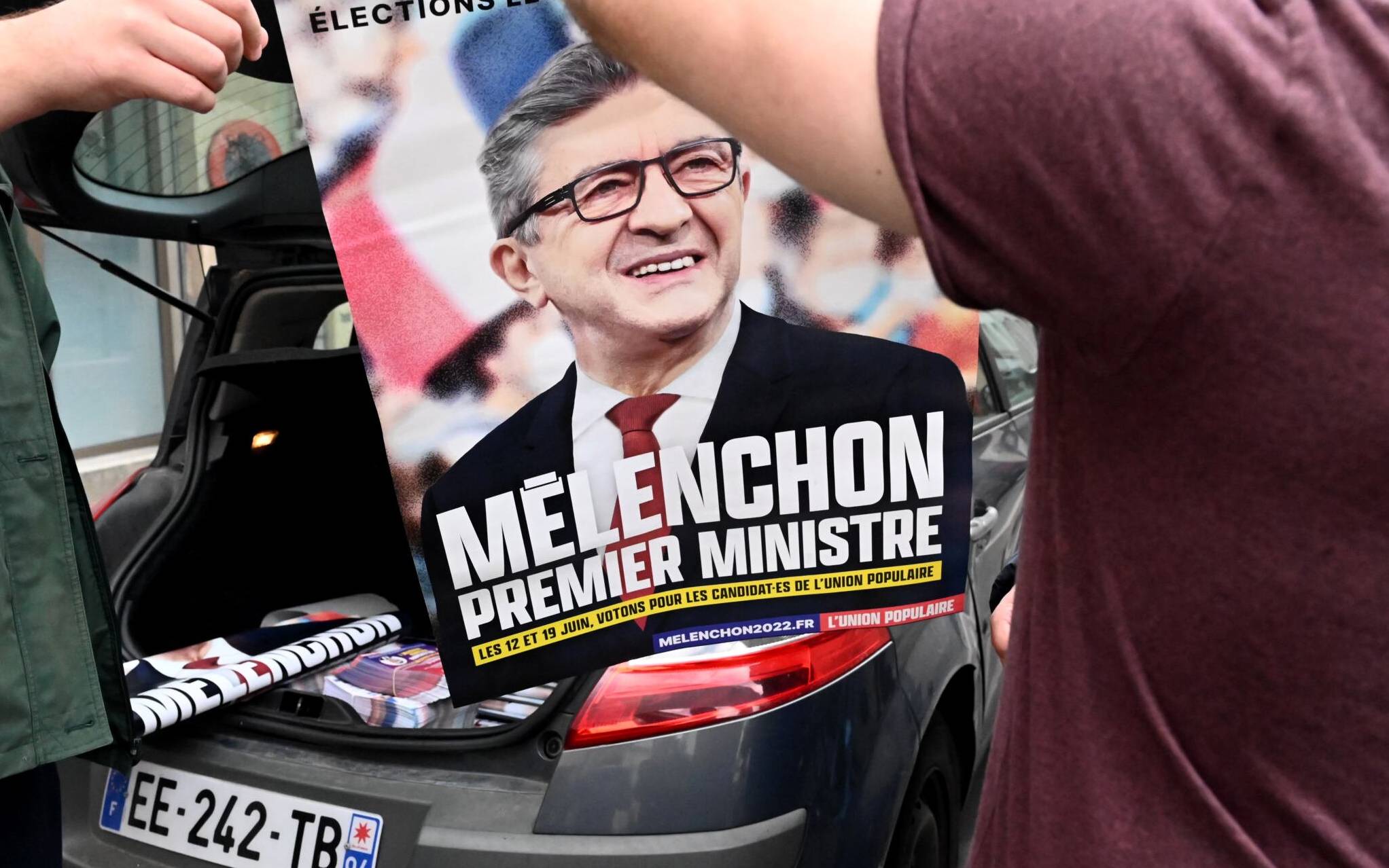 Militants of French leftist movement La France Insoumise (LFI) display a campaign poster reading in French "Melenchon, Prime Minister" outside LFI's headquarters in Paris on May 3, 2022, where discussions are underway on a broad alliance between the four main leftists parties for June parliamentary polls. (Photo by EMMANUEL DUNAND / AFP)