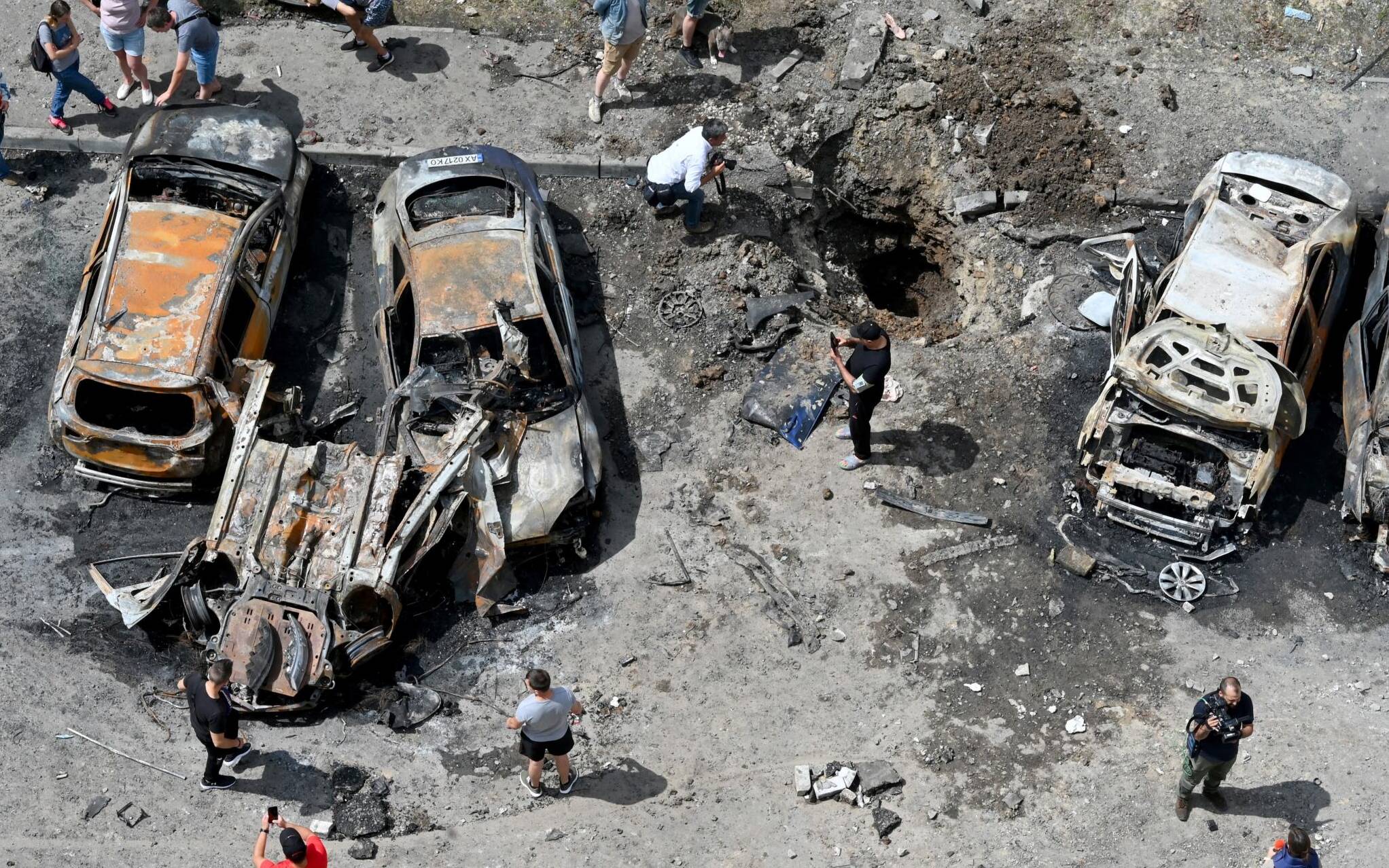 Bystanders gather around the wreckage of vehicles and a crater after Russian missiles struck the courtyard of a multi-storey residential complex on the eastern outskirts of Kharkiv on June 26, 2022, amid the Russian invasion of Ukraine. (Photo by SERGEY BOBOK / AFP)