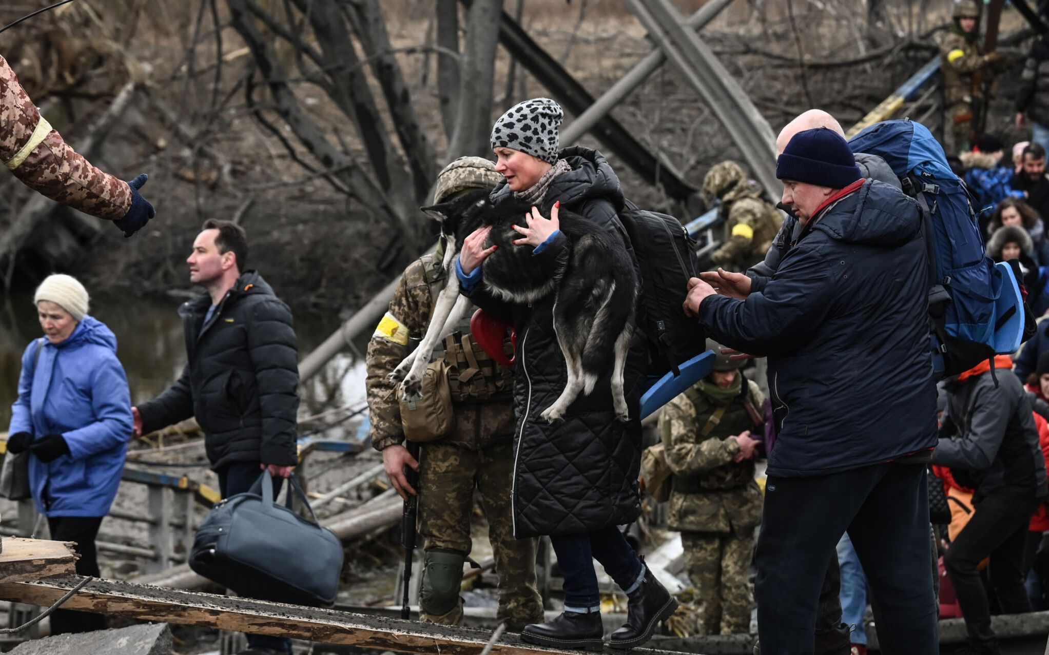A woman carries a dog  while people cross a destroyed bridge as they  evacuate the city of Irpin, northwest of Kyiv, during heavy shelling and bombing on March 5, 2022, 10 days after Russia launched a military in vasion on Ukraine. (Photo by Aris Messinis / AFP)