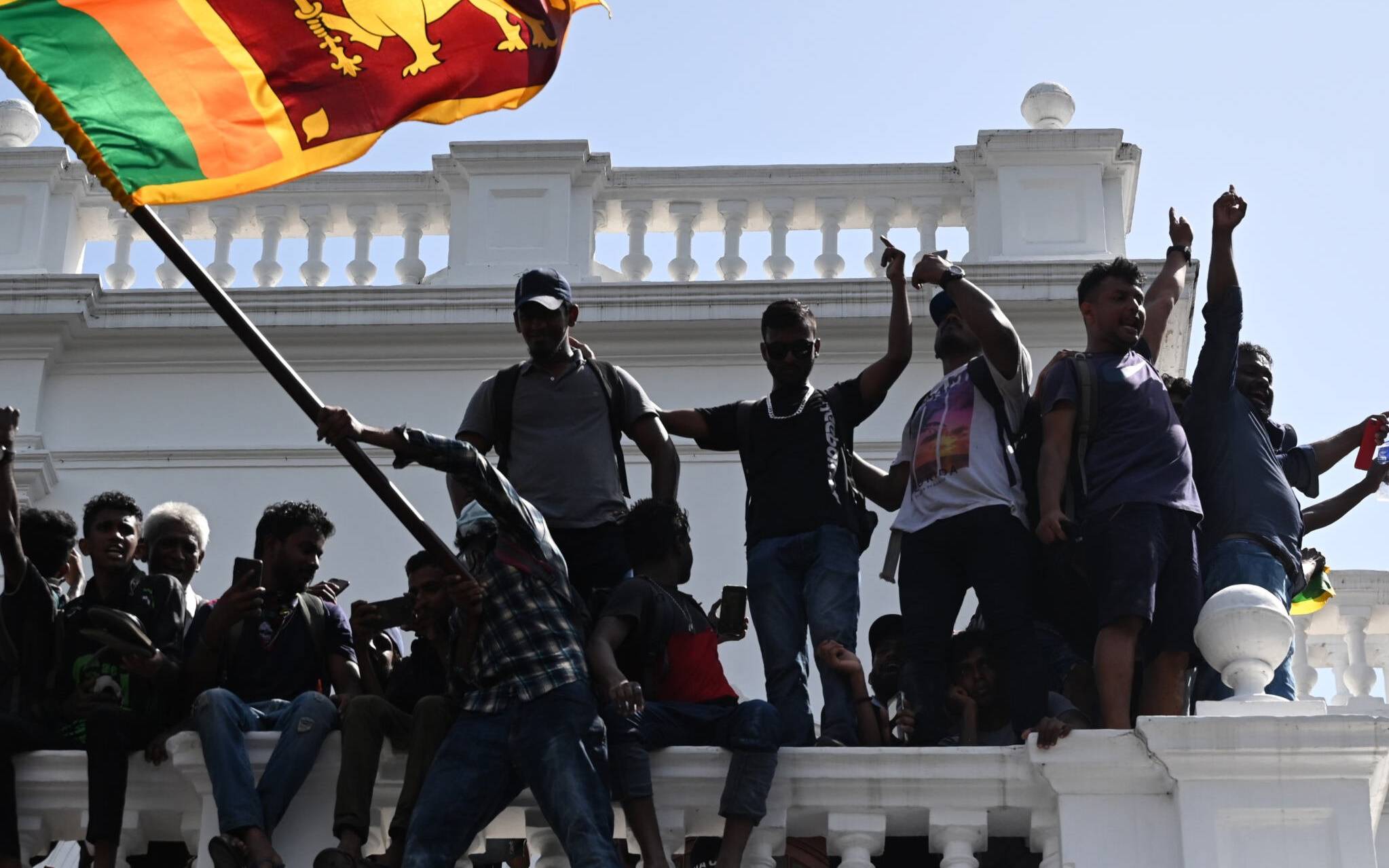 Demonstrators shout slogans and wave Sri Lankan flags from a balcony during an anti-government protest inside the office building of Sri Lanka's prime minister in Colombo on July 13, 2022. - Thousands of anti-government protesters stormed into Sri Lanka Prime Minister Ranil Wickremesinghe's office on July 13, hours after he was named as acting president, witnesses said. (Photo by Arun SANKAR / AFP)