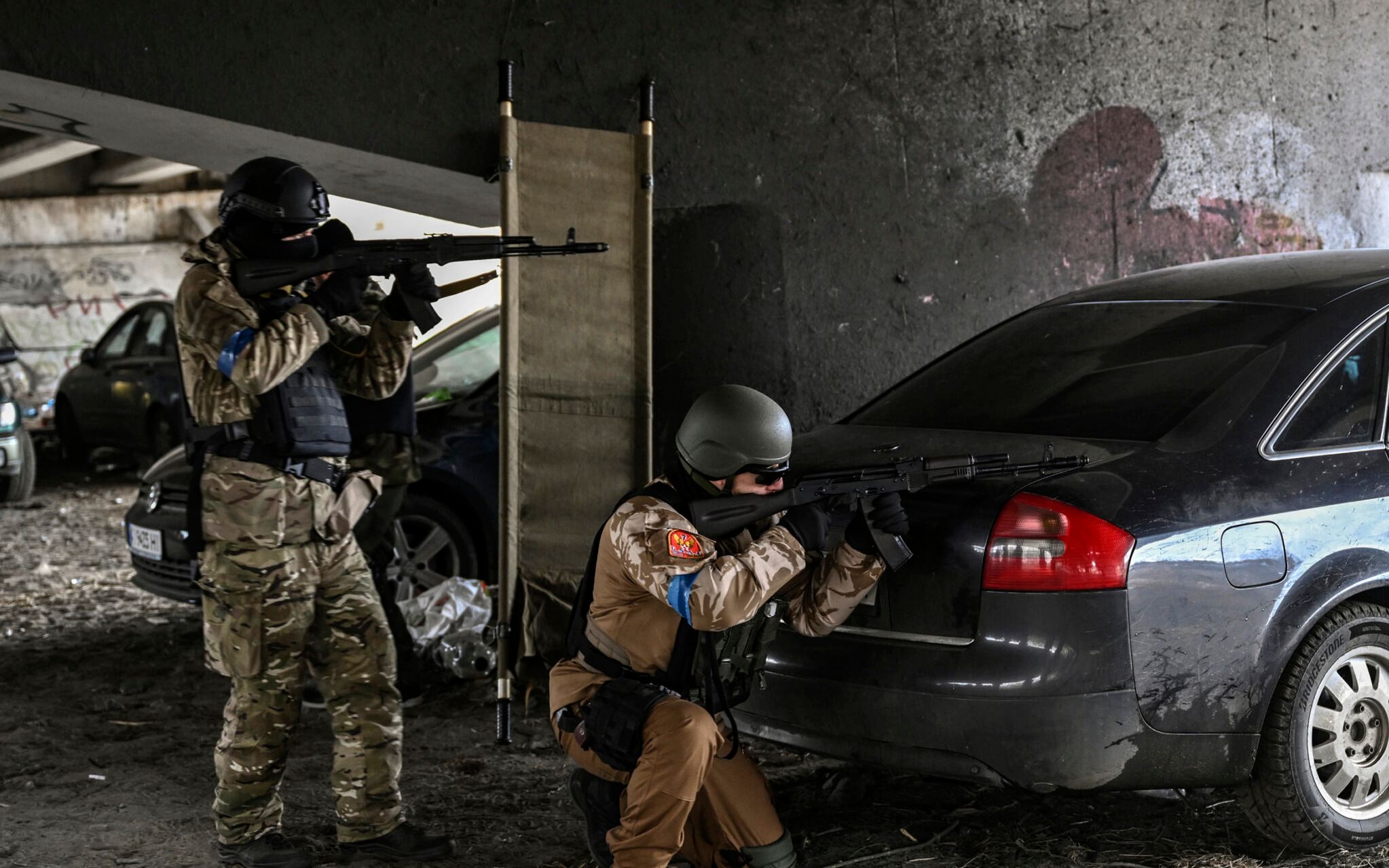 Ukrainian servicemen aim with their weapons at a moving car from a postition under a destroyed bridge in the city of Irpin, northwest of Kyiv, on March 13, 2022. - Russian forces advance ever closer to the capital from the north, west and northeast. Russian strikes also destroy an airport in the town of Vasylkiv, south of Kyiv. A US journalist was shot dead and another wounded in Irpin, a frontline northwest suburb of Kyiv, medics and witnesses told AFP. (Photo by Aris Messinis / AFP)