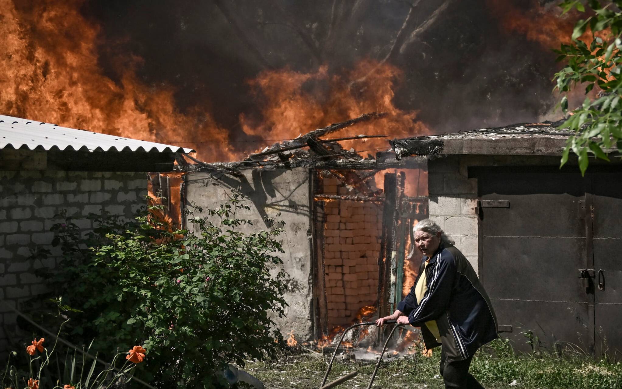 An elderly woman walks away from a burning house garage after shelling in the city of Lysytsansk at the eastern Ukrainian region of Donbas on May 30, 2022, on the 96th day of the Russian invasion of Ukraine. - Since failing to capture Kyiv in the war's early stages, Russia's army has narrowed its focus, hammering Donbas cities with artillery and missile barrages as it seeks to consolidate its control. (Photo by ARIS MESSINIS / AFP)