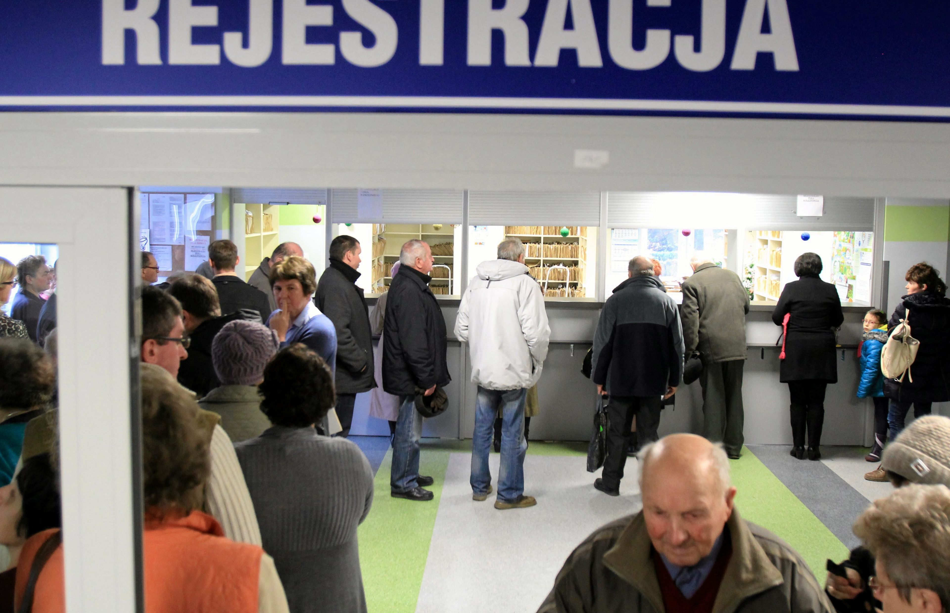 Kolejka ludzi stoi pod napisem (na ciemnoniebieskim tle) REJESTRACJA