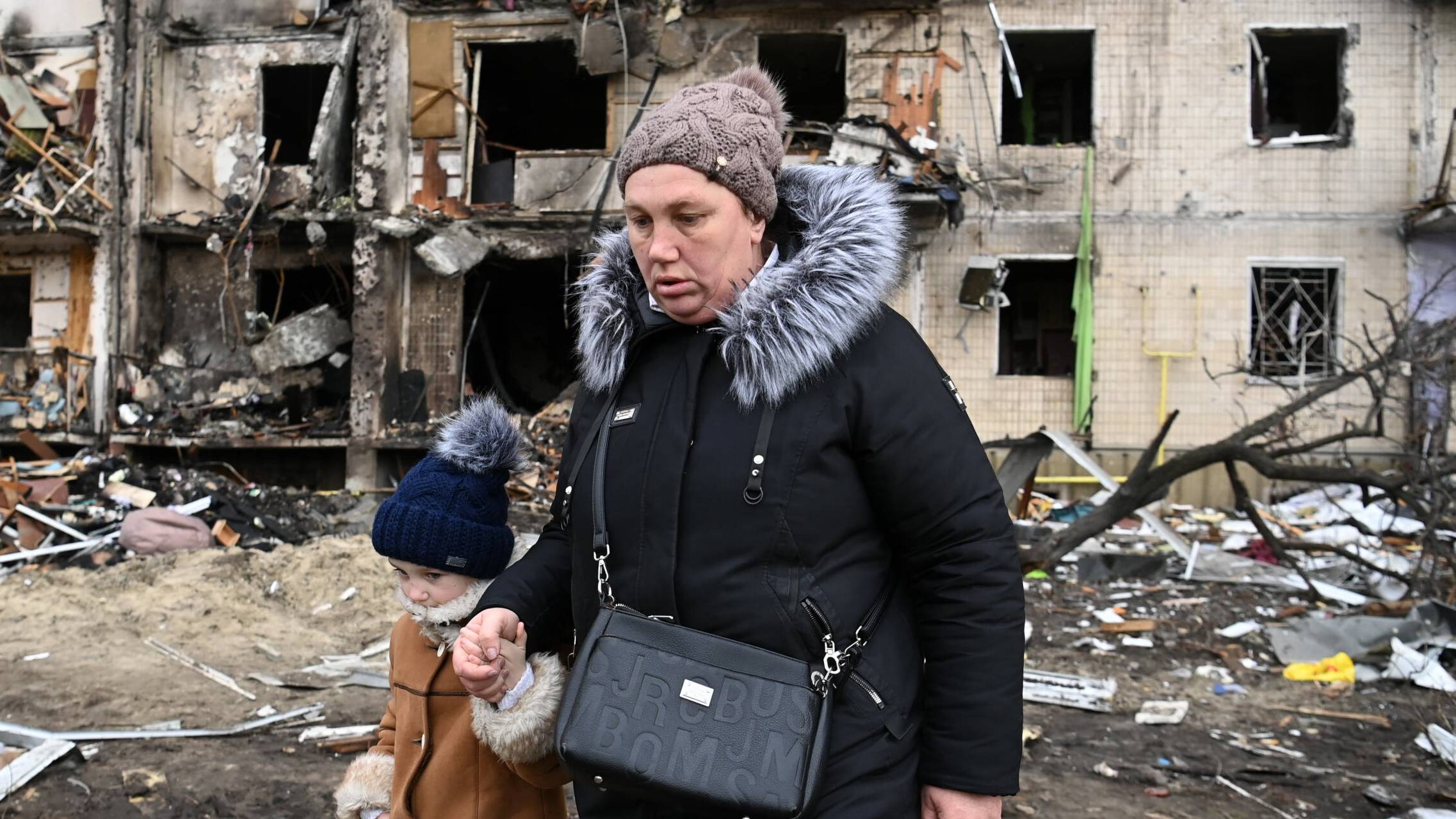 Ukraina. Matka z dzieckiem przed zniszczonym przez Rosjan blokiem mieszkalnym w Kijowie