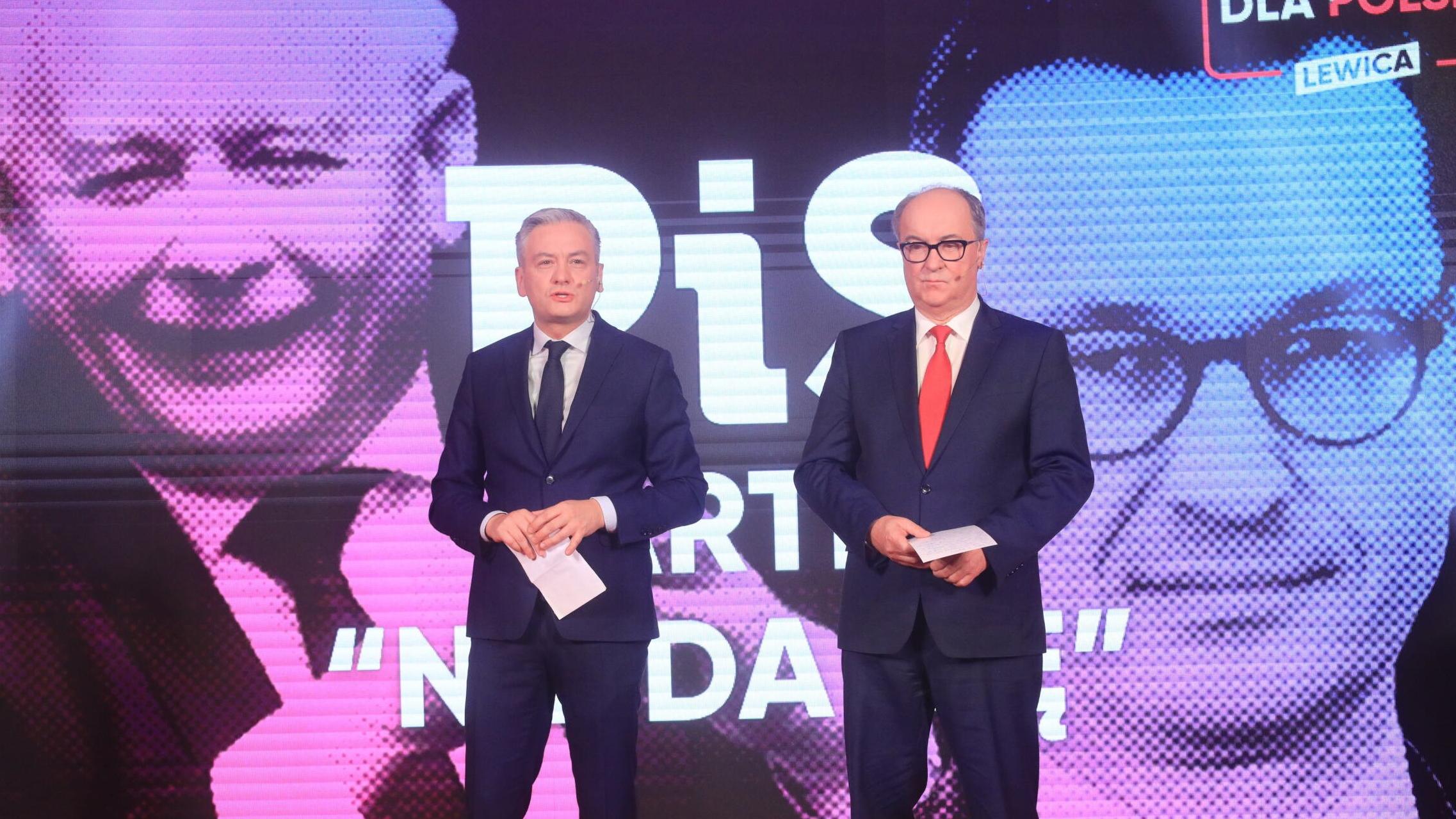 Dwaj mężczyźni (Czarzasty i Biedroń) na scenie, w tle portrety Kaczyńskiego i Morawieckiego