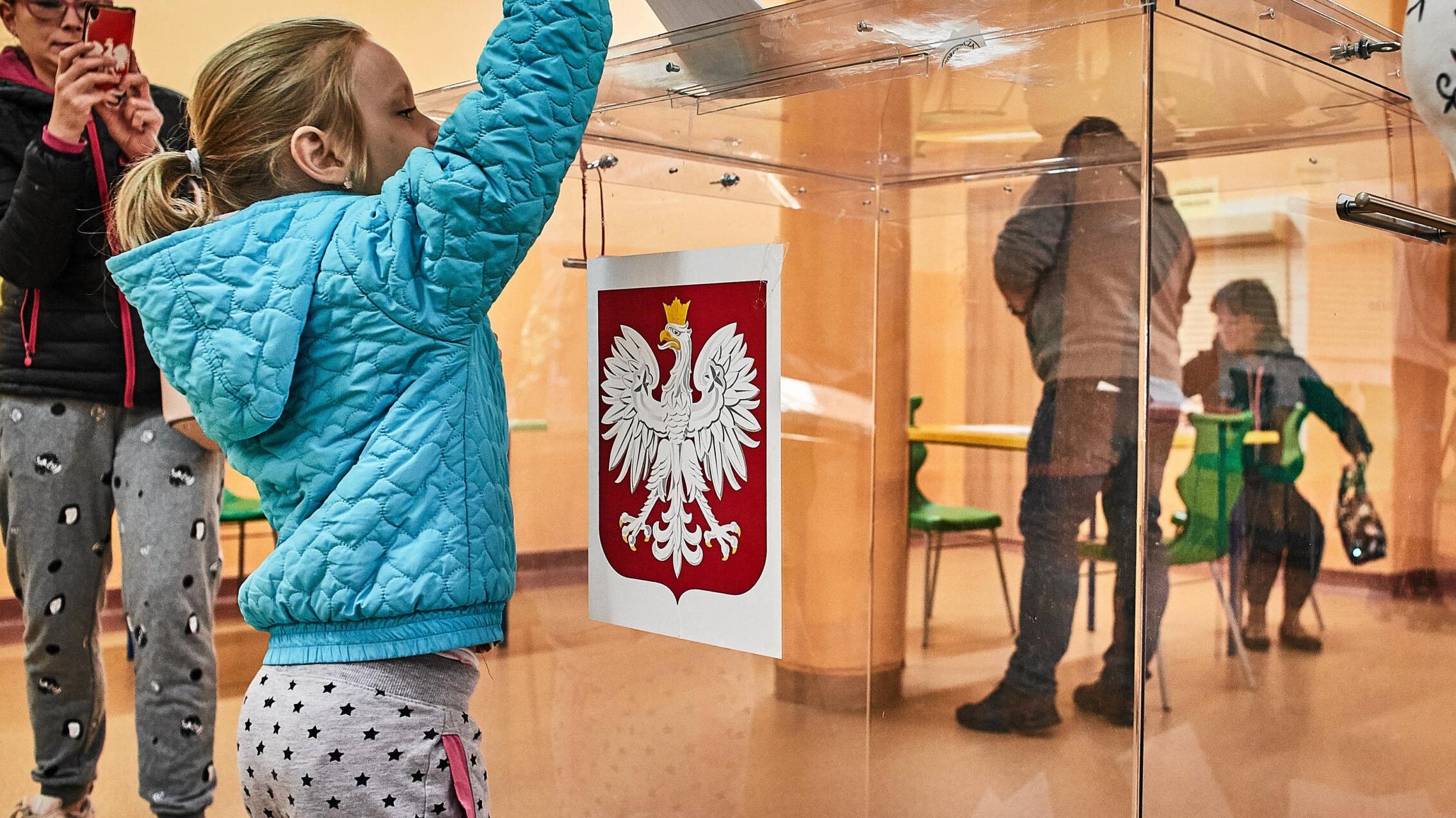 Dziewczynka wspina się na palce, żeby wrzucić głos do urny wyborczej