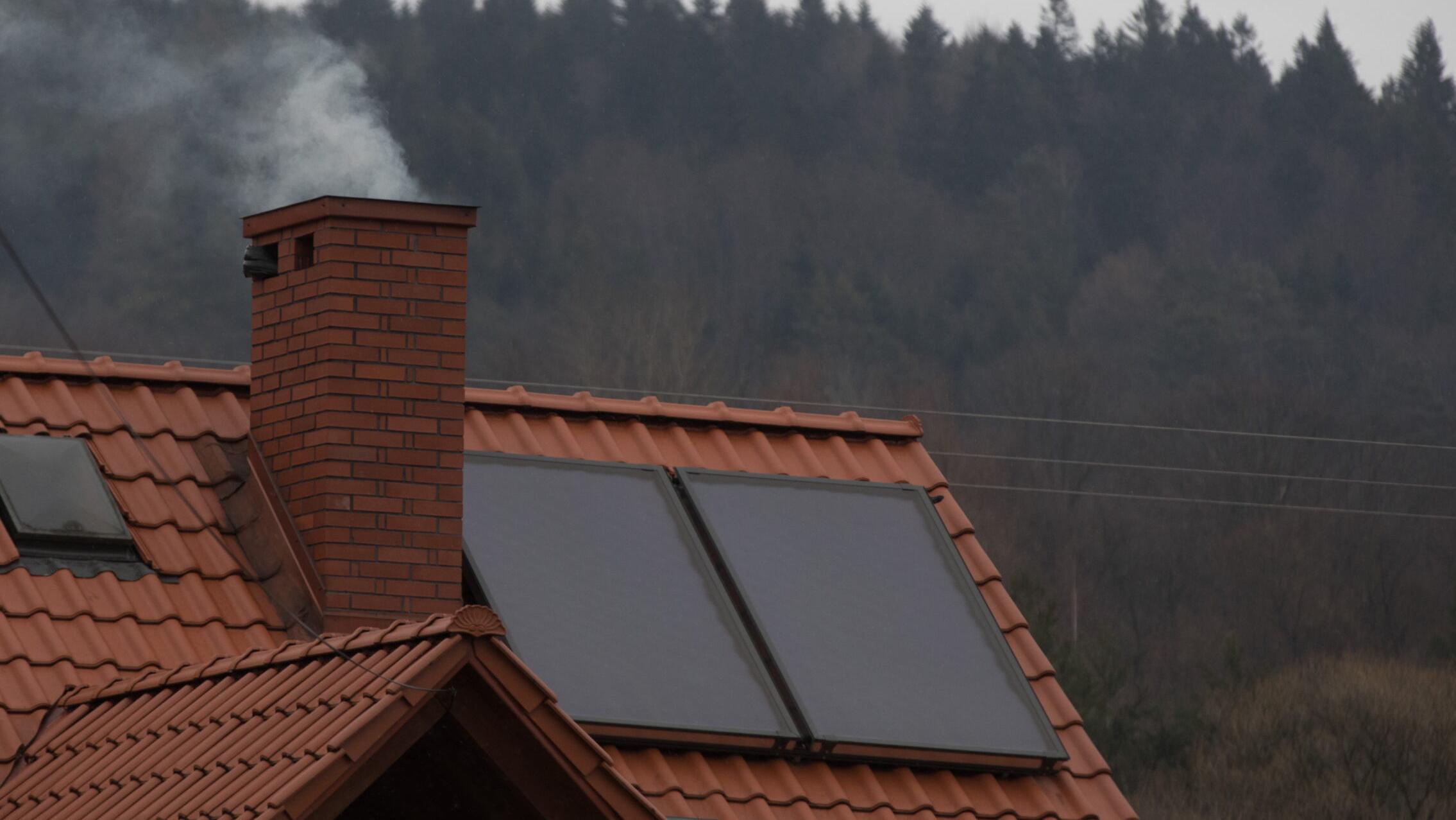 Dym z komina - dach, obok komina dwa panele słoneczne