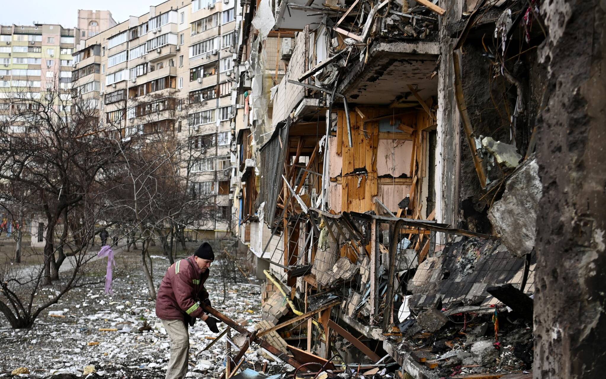 A man clears debris at a damaged residential building at Koshytsa Street, a suburb of the Ukrainian capital Kyiv, where a military shell allegedly hit, on February 25, 2022. - Russian forces reached the outskirts of Kyiv on Friday as Ukrainian President Volodymyr Zelensky said the invading troops were targeting civilians and explosions could be heard in the besieged capital. Pre-dawn blasts in Kyiv set off a second day of violence after Russian President Vladimir Putin defied Western warnings to unleash a full-scale ground invasion and air assault on Thursday that quickly claimed dozens of lives and displaced at least 100,000 people. (Photo by Daniel LEAL / AFP)