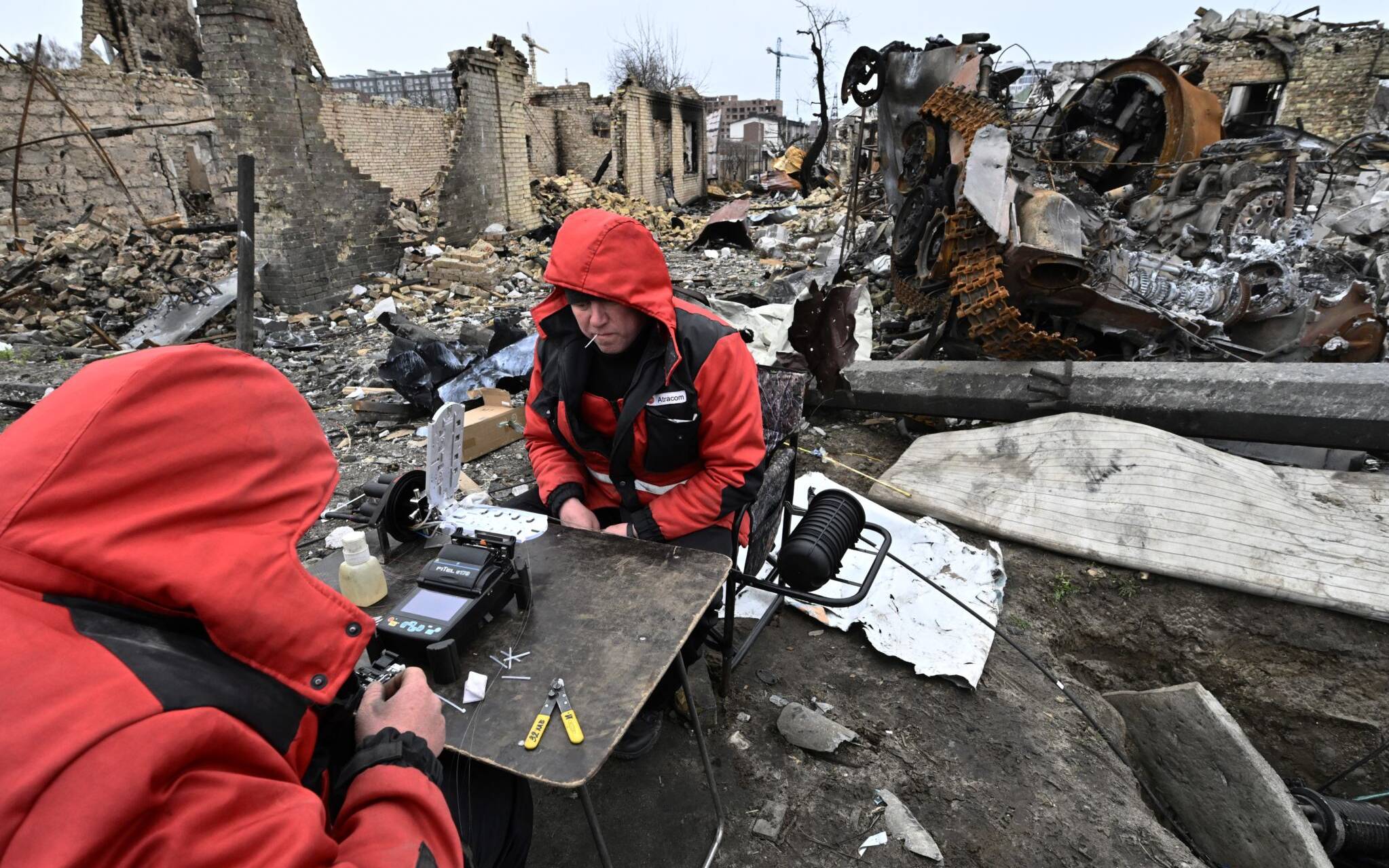 Repairmen restore local communication cables among the debris of destroyed armoured vehicles and buildings on a street in the town of Bucha, on the outskirts of the Ukrainian capital Kyiv on April 5, 2022. (Photo by Genya SAVILOV / AFP)