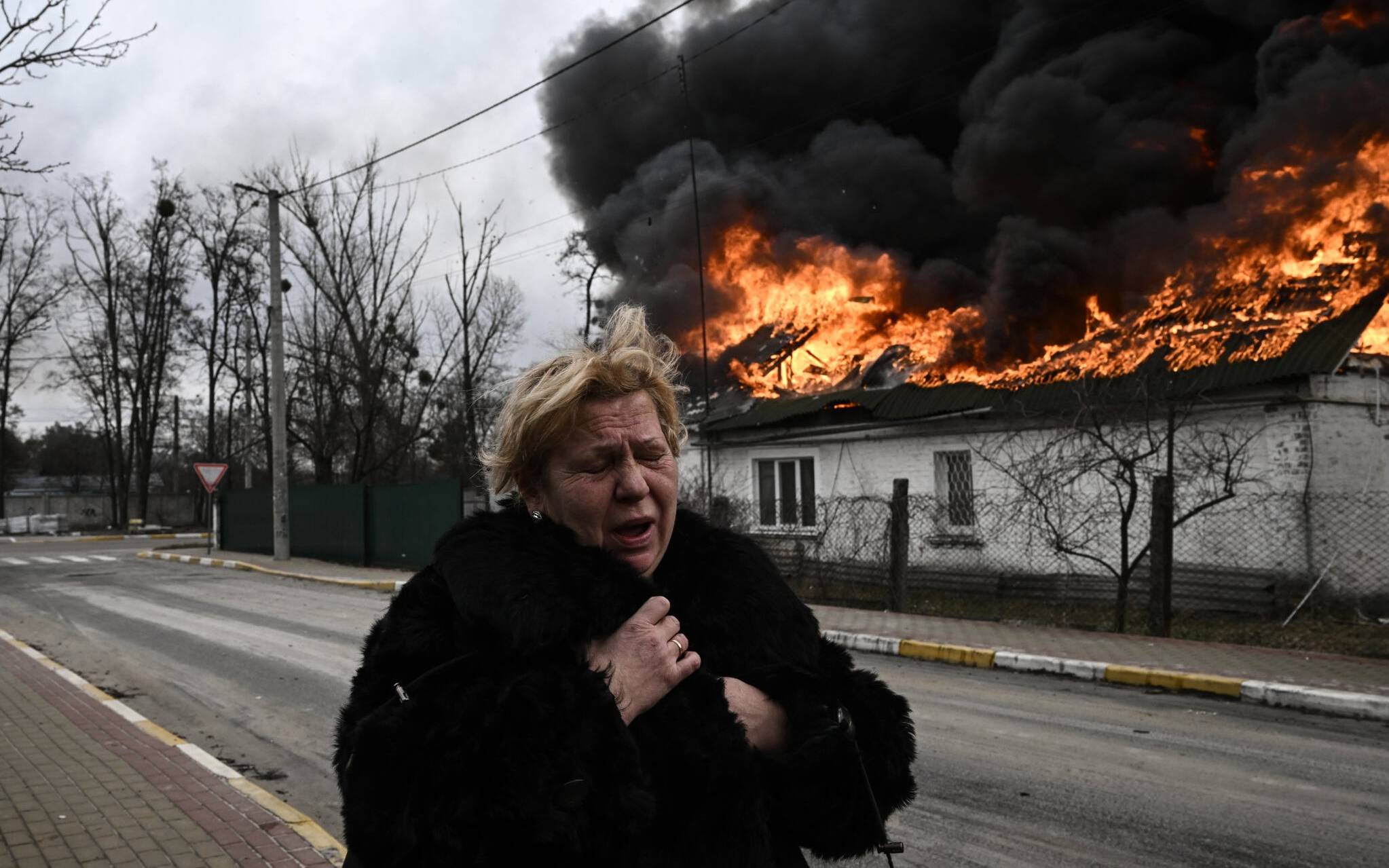 A woman reacts as she stands in front of a house burning after being shelled in the city of Irpin, outside Kyiv, on March 4, 2022. - More than 1.2 million people have fled Ukraine into neighbouring countries since Russia launched its full-scale invasion on February 24, United Nations figures showed on March 4, 2022. (Photo by Aris Messinis / AFP)