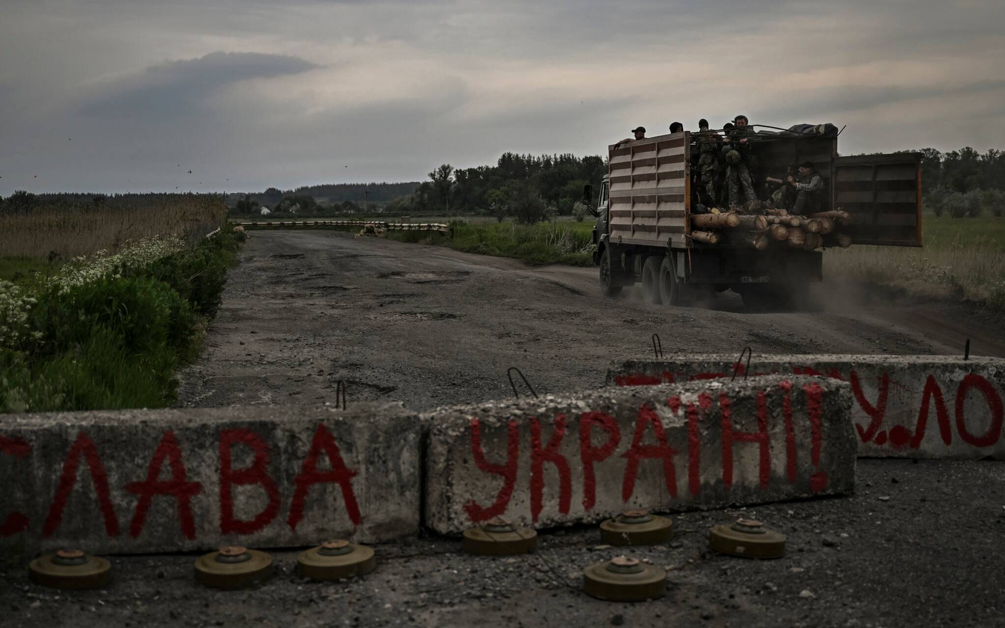 A truck with Ukrainian servicemen drives by a roadblock, with ant-tank mines, inscribed Glory to Ukraine outside the city of Barvinkove in the eastern Ukrainian region of Donbas, on May 29, 2022. (Photo by Aris Messinis / AFP)