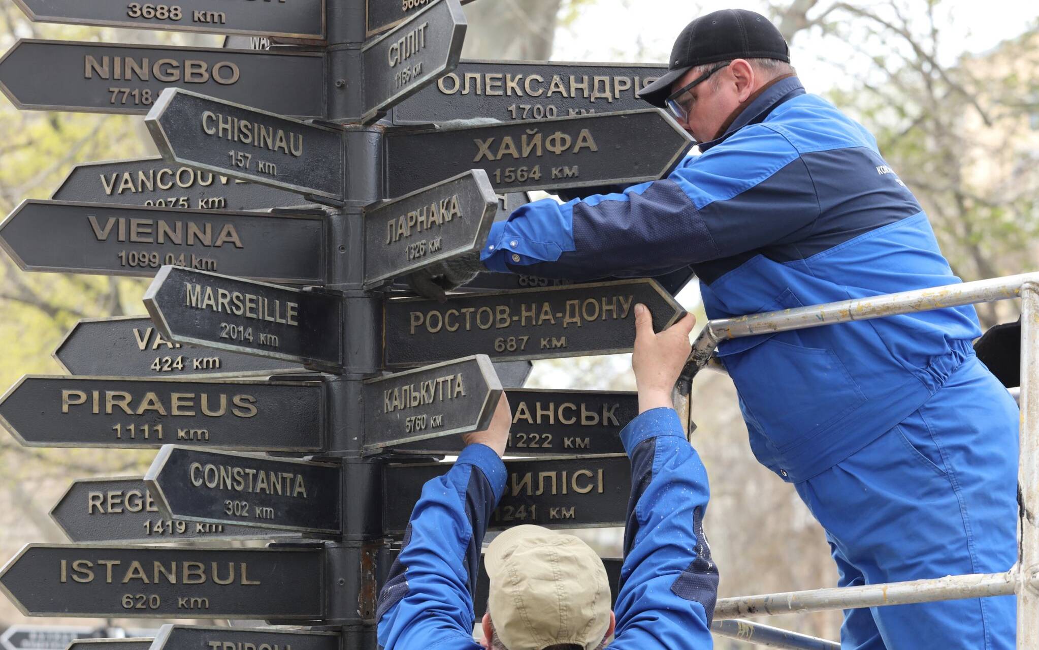 Communal sevices workers dismantle plates bearing the names of Russian cities from a decorative street sign indicating directions and distances of Odessa's sister cities, in the centre of the Ukrainian Black Sea port of Odessa on April 14, 2022, amid Russia's military invasion launched on Ukraine. (Photo by Oleksandr GIMANOV / AFP)