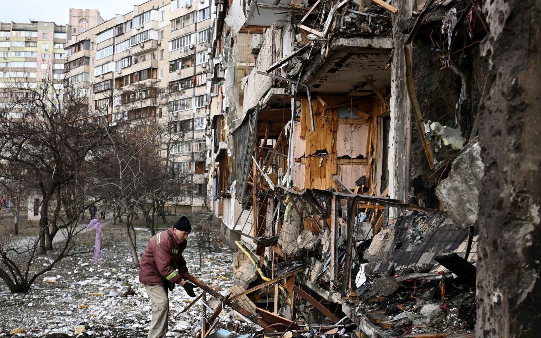 A man clears debris at a damaged residential building at Koshytsa Street, a suburb of the Ukrainian capital Kyiv, where a military shell allegedly hit, on February 25, 2022. - Russian forces reached the outskirts of Kyiv on Friday as Ukrainian President Volodymyr Zelensky said the invading troops were targeting civilians and explosions could be heard in the besieged capital. Pre-dawn blasts in Kyiv set off a second day of violence after Russian President Vladimir Putin defied Western warnings to unleash a full-scale ground invasion and air assault on Thursday that quickly claimed dozens of lives and displaced at least 100,000 people. (Photo by Daniel LEAL / AFP)