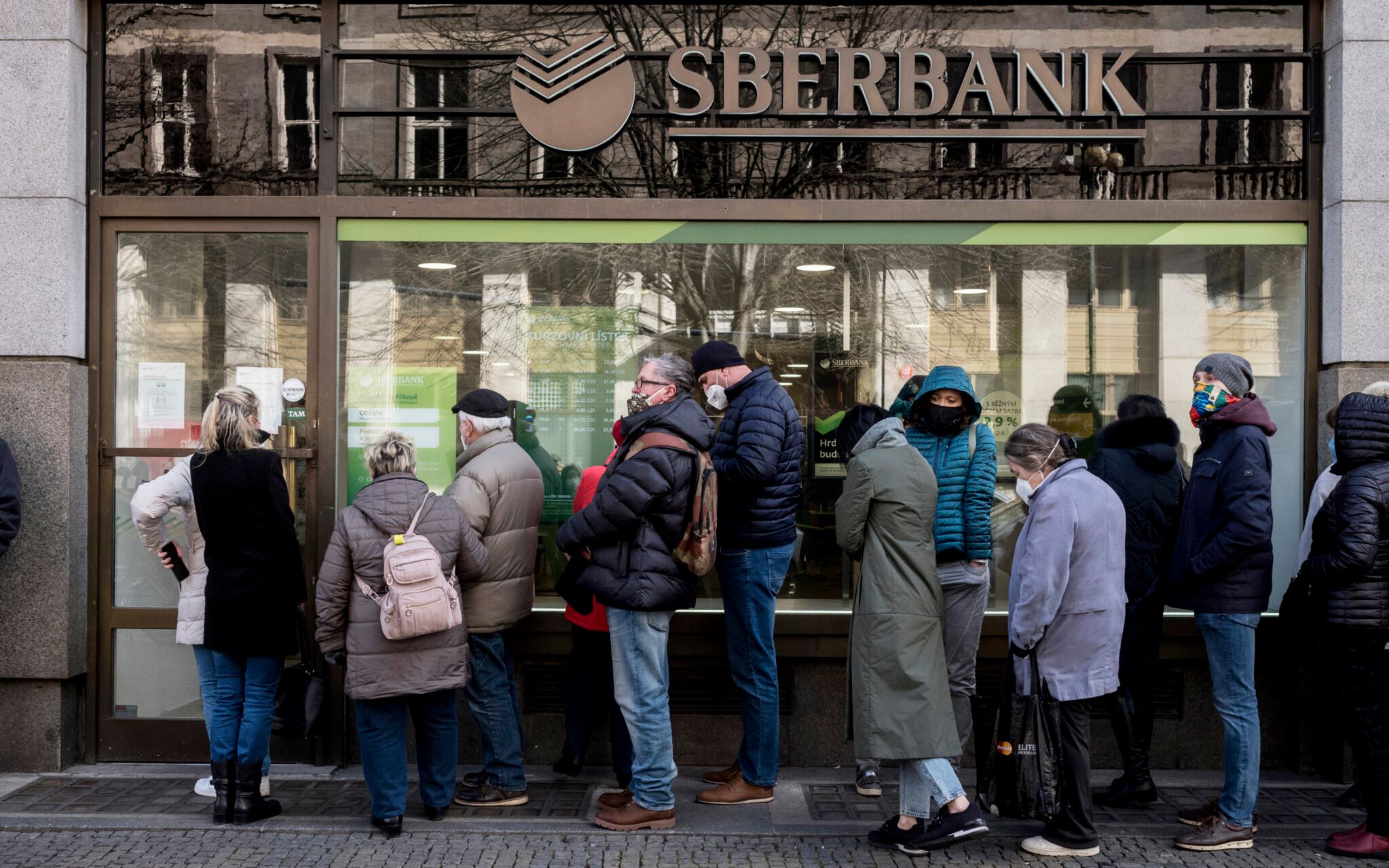 People queue outside a branch of Russian state-owned bank Sberbank to withdraw their savings and close their accounts in Prague on February 25, 2022, before Sberbank will close all its branches in the Czech Republic later in the day. - US President Biden was the first to announce sanctions, hours after Russian President Putin declared a "military operation" into Ukraine. The first tranche will hit four Russian banks -- including the country's two largest, Sberbank and VTB Bank -- cut off more than half of Russia's technology imports, and target several of the country's oligarchs. (Photo by Michal Cizek / AFP)