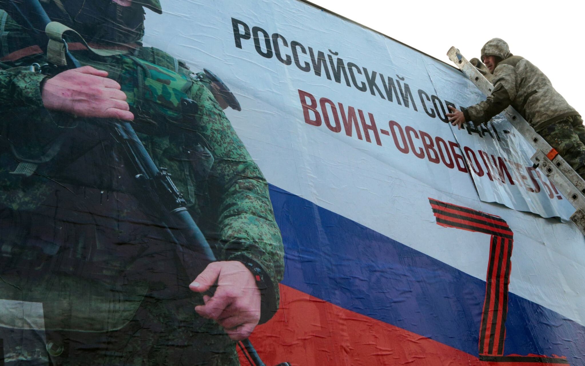 A man finishes glueing a huge placard depicting a serviceman and reading "A Russian soldier is a liberator!" in the city center of Simferopol, Crimea, on March 4, 2022. - Ukraine accused the Kremlin of "nuclear terror" on March 4, after Europe's largest atomic power plant was attacked and taken over by invading forces, sparking Western horror at the threat of Russia's war contaminating all of Europe. (Photo by STRINGER / AFP)