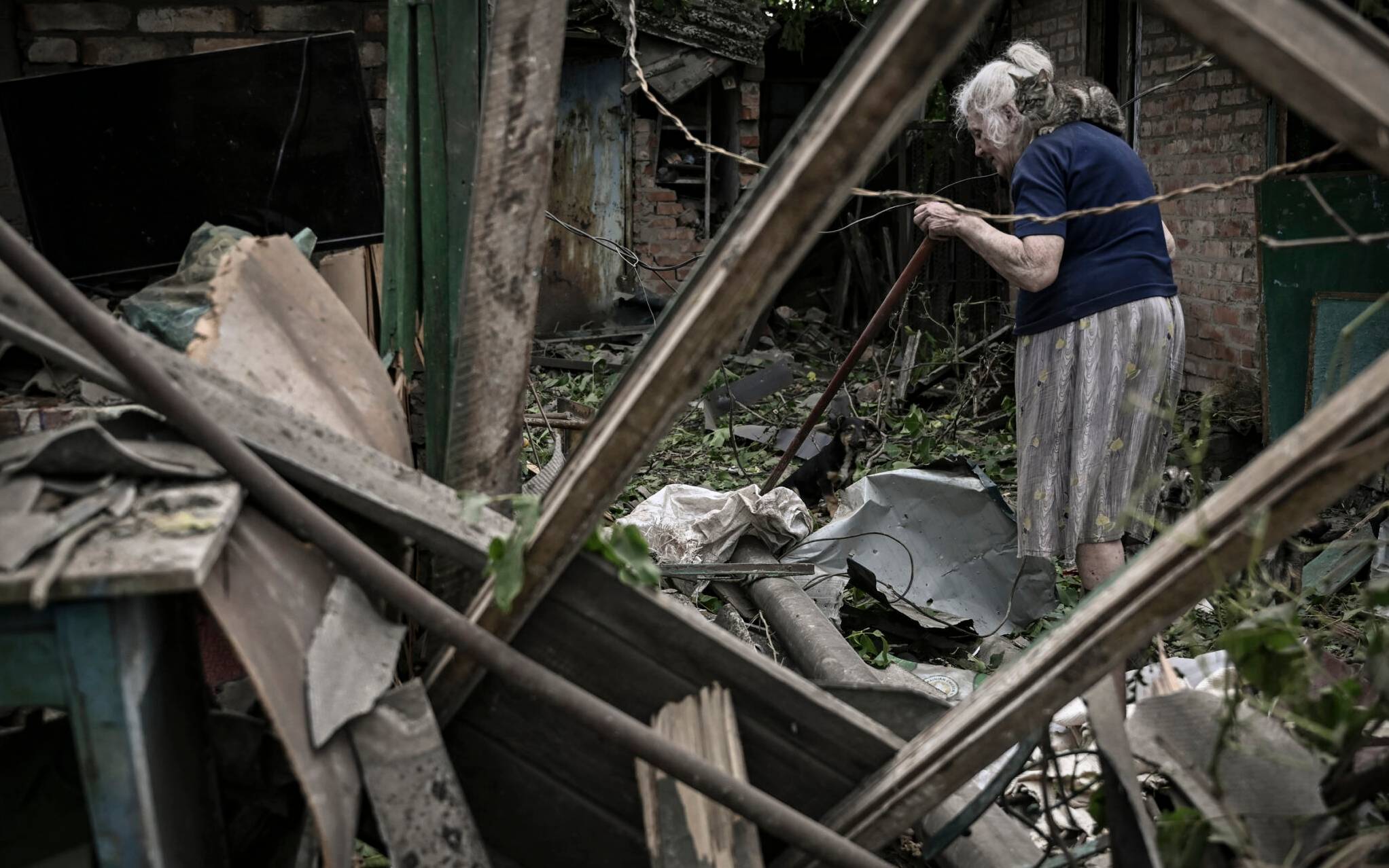 An eldery woman, with a cat on her shoulder, tries to clean her yard from debris after a missile strike killing one old woman in the city of Droujkivka at the eastern Ukrainian region of Donbas on June 5, 2022. (Photo by ARIS MESSINIS / AFP)