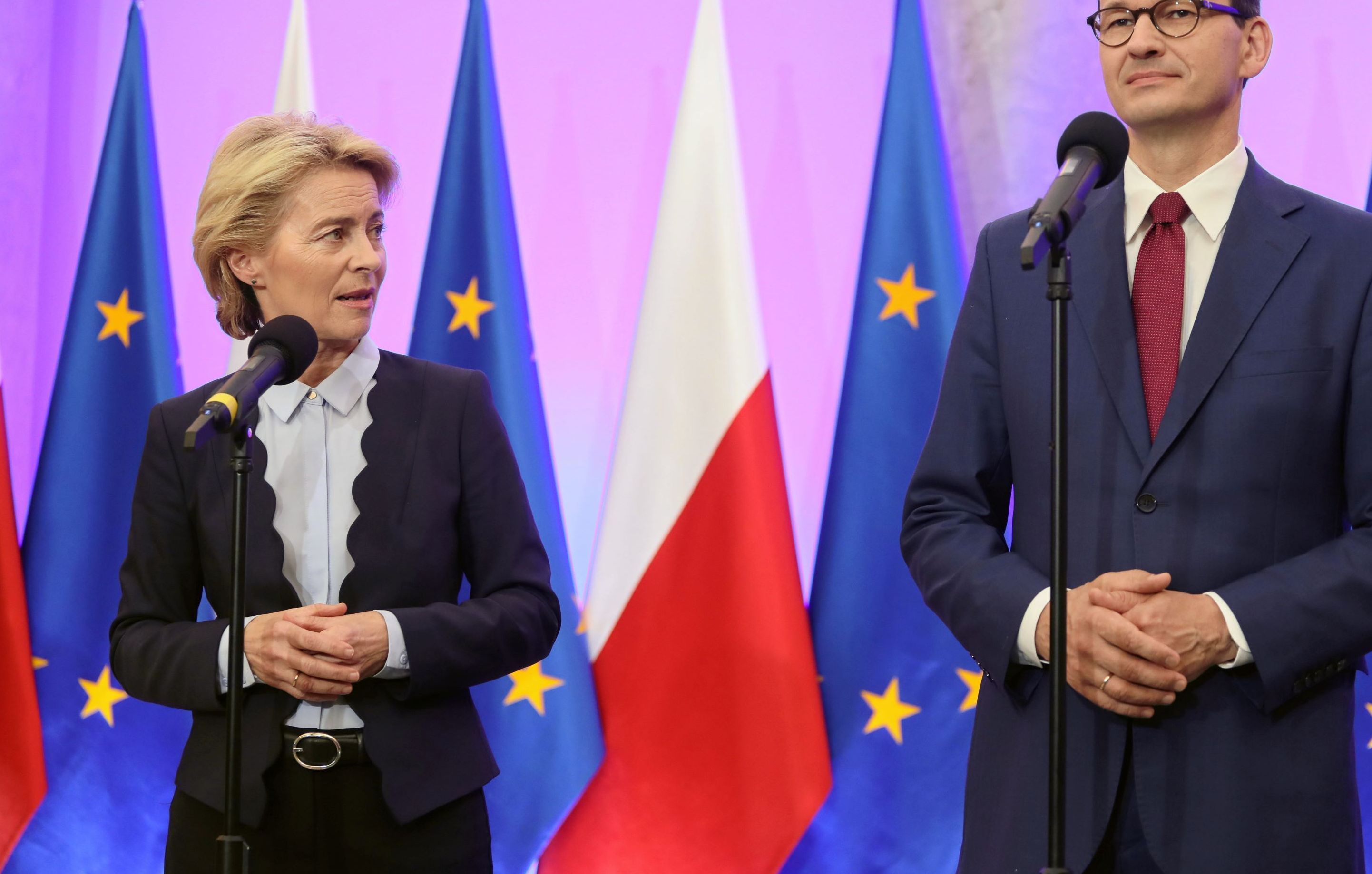 Mateusz Morawiecki i Ursula von der Leyen stoją na tle flag polskich i europejskich.